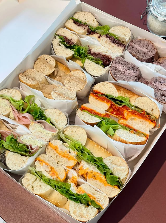 A box of various mini sandwiches including turkey, ham, chicken salad, tuna salad, and veggie options, with different breads and toppings.