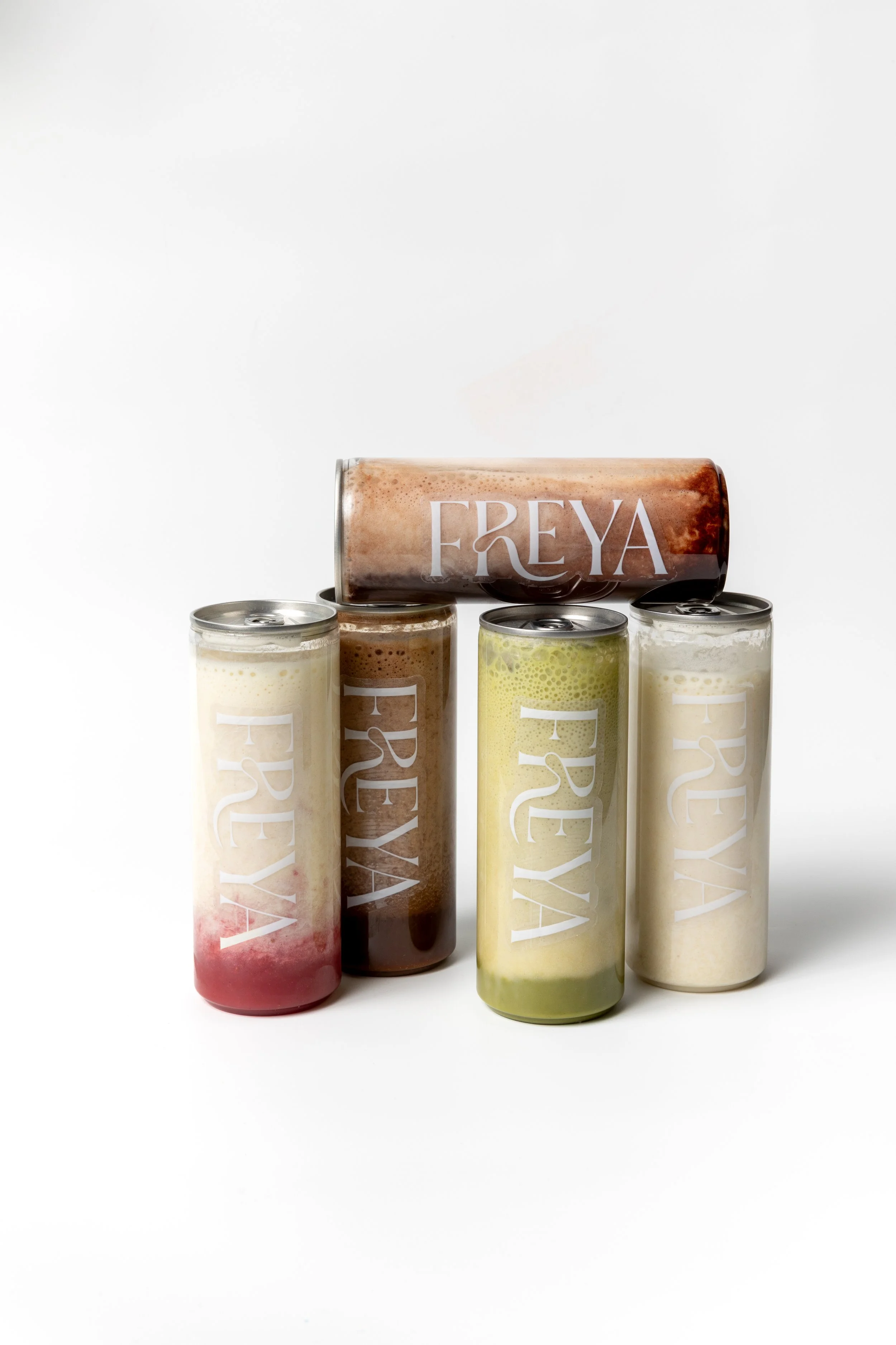 Five cans of Freya beverages, featuring various flavors, arranged on a white background with one can placed horizontally on top of the others.