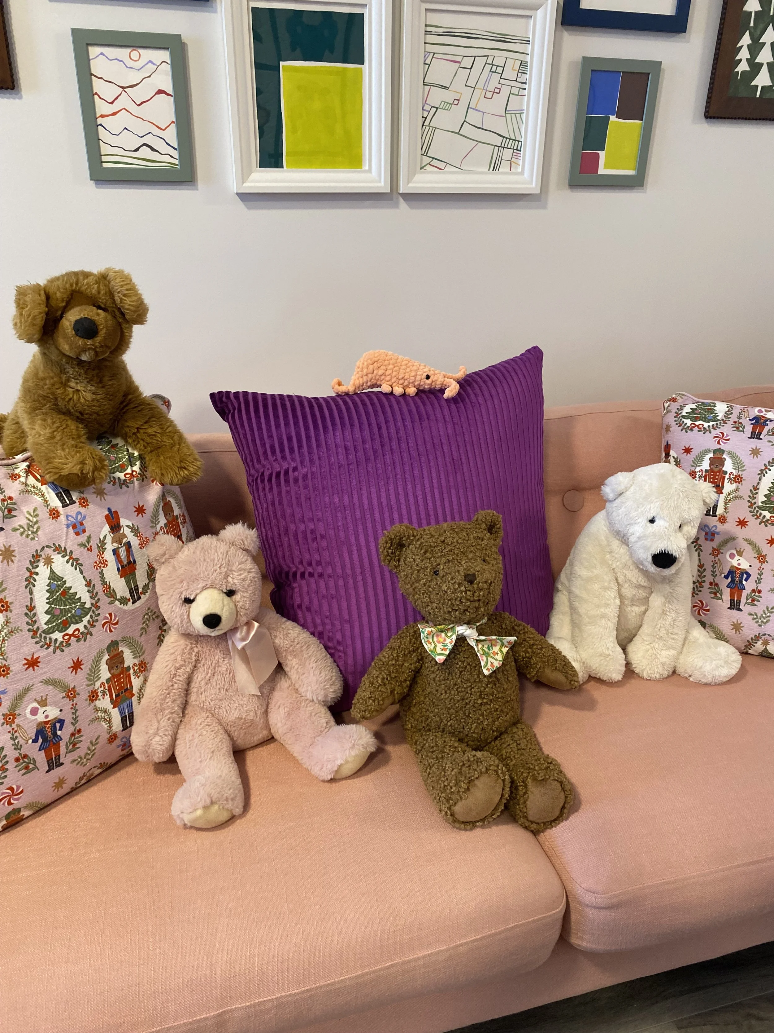 Stuffed animals sitting on a pink sofa surrounded by pillows.