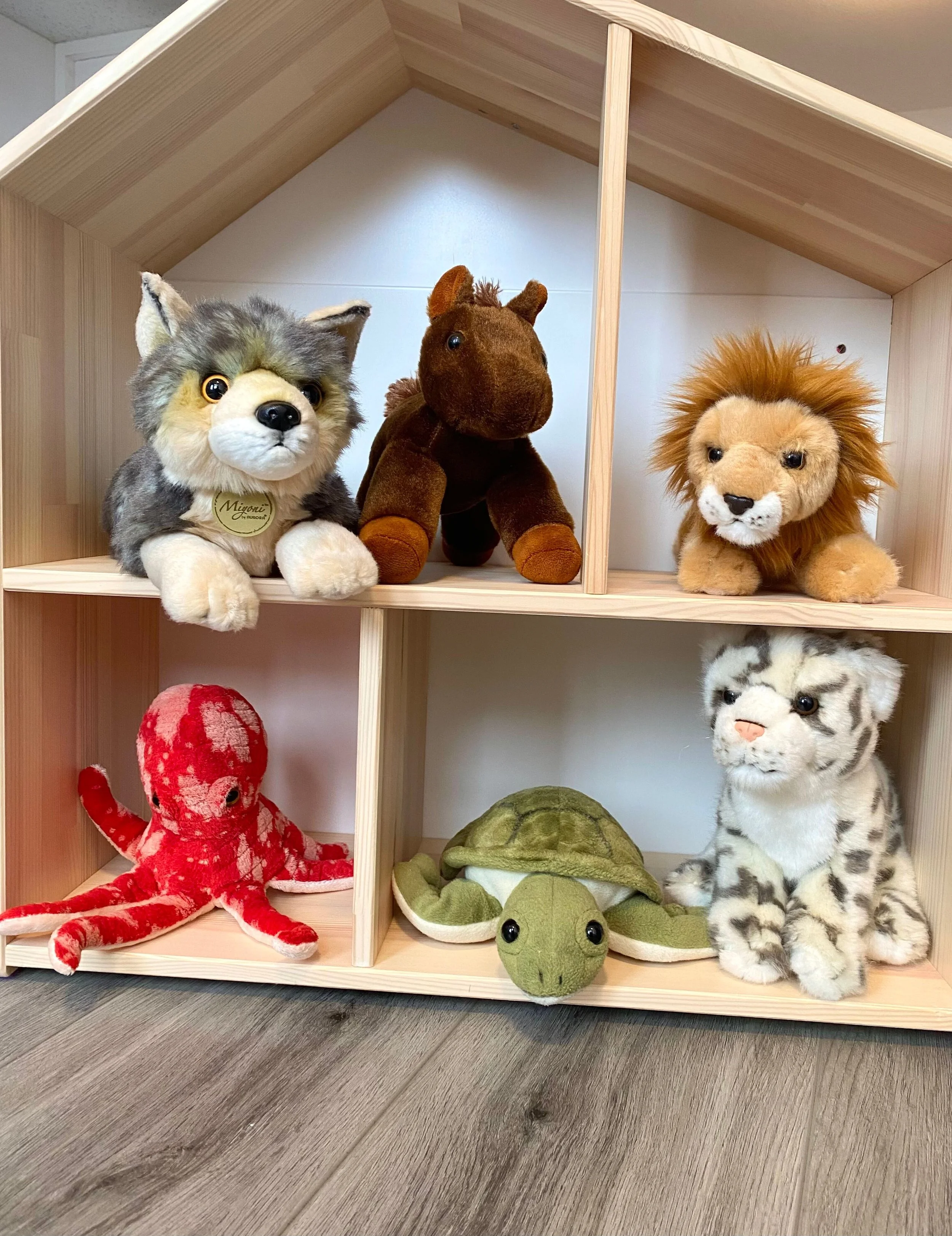 A doll house with stuffed animals in it, such as a lion and a wolf.