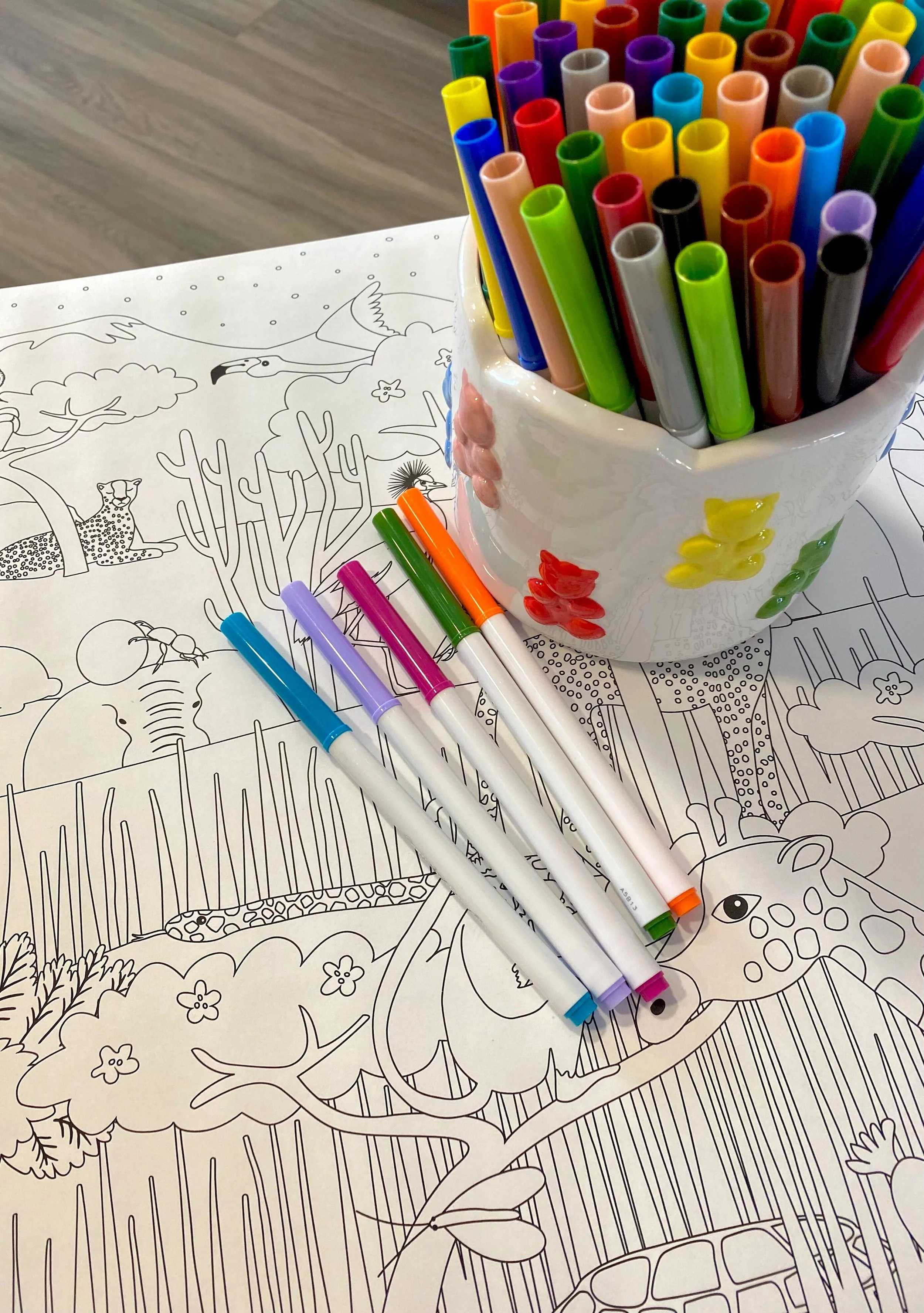 Markers in a container on top of a colouring page.