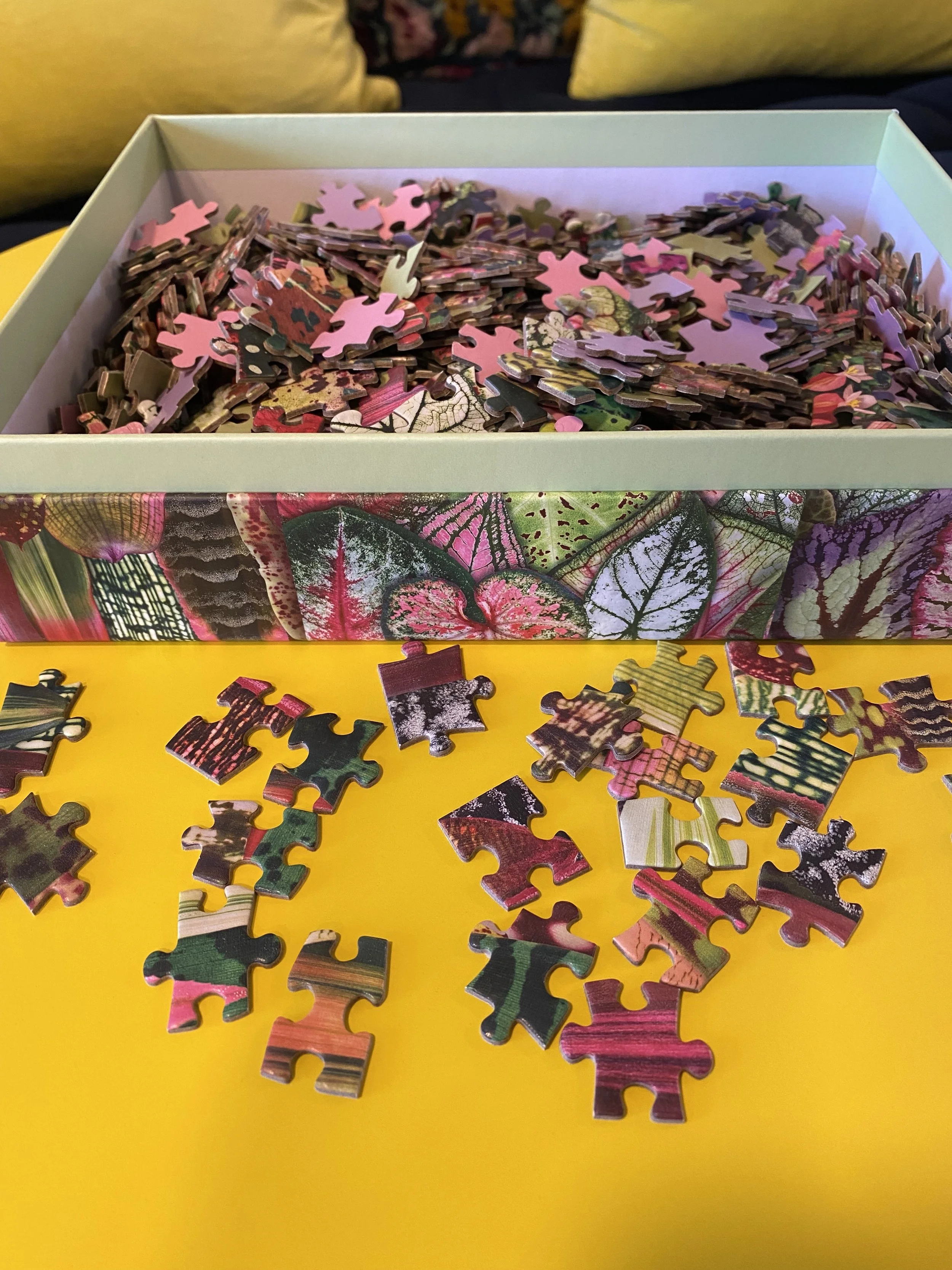 A box of puzzle pieces on a yellow table.