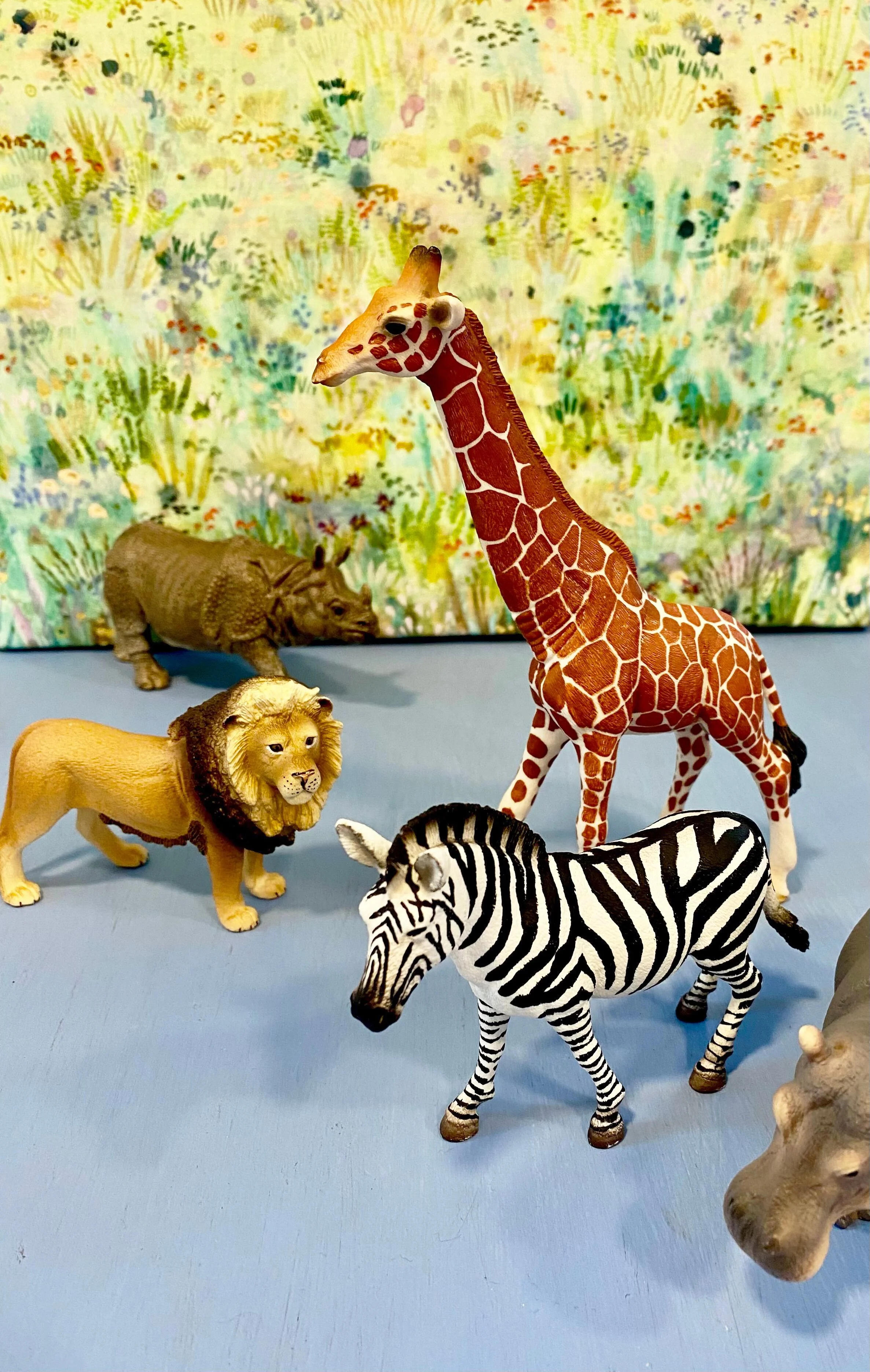 Plastic toy safari animals on a table with a nature fabric background.