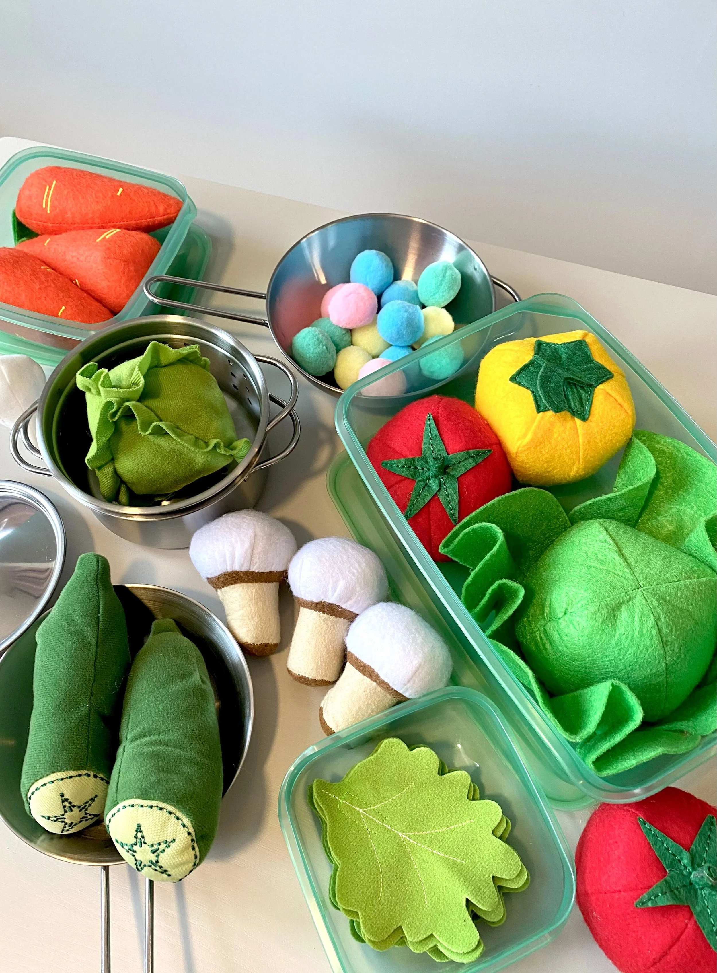 Felt and fabric pretend vegetables in toy cooking dishes.