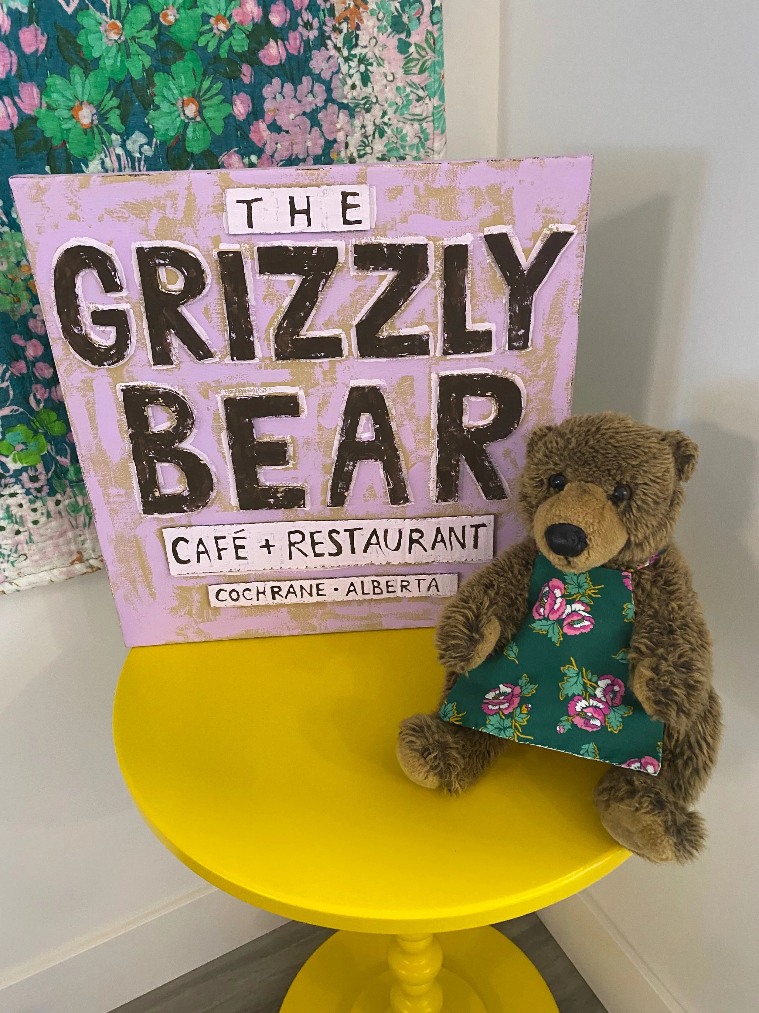 A canvas sign on a yellow table that says The Grizzly Bear Cafe and Restaurant.