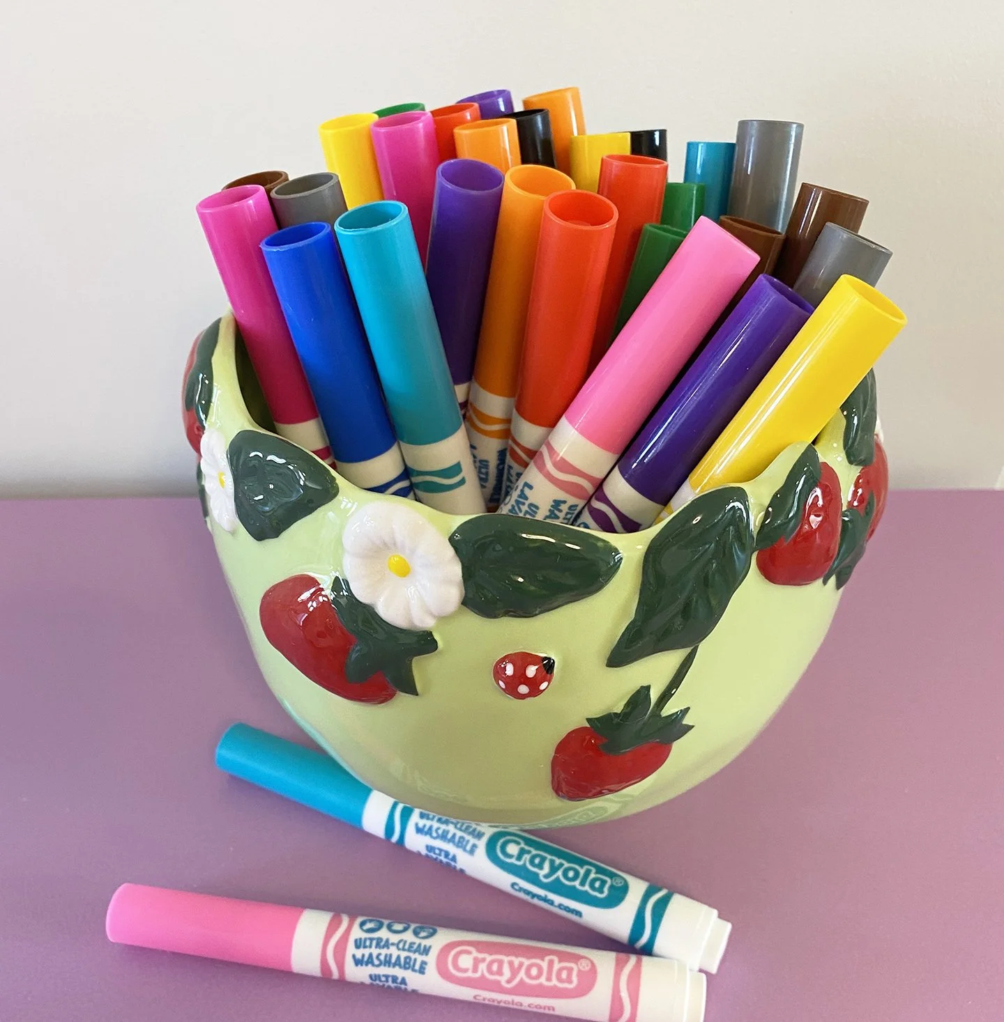 A container of colourful markers on a pink table.