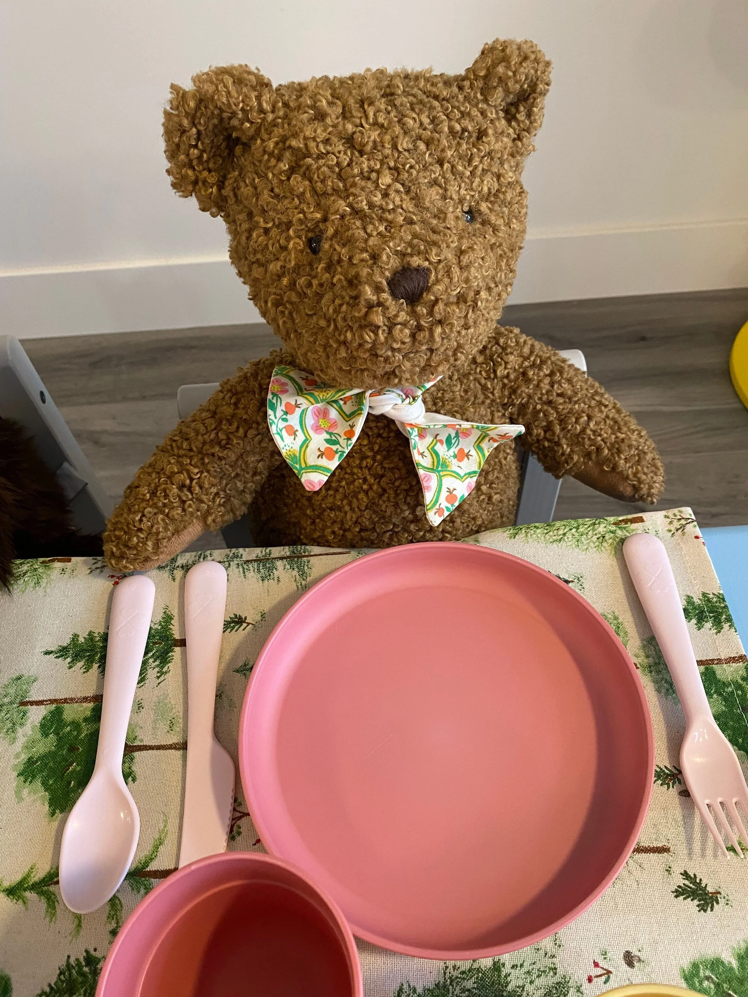A teddy bear sitting at a table with a pink plate and cup.