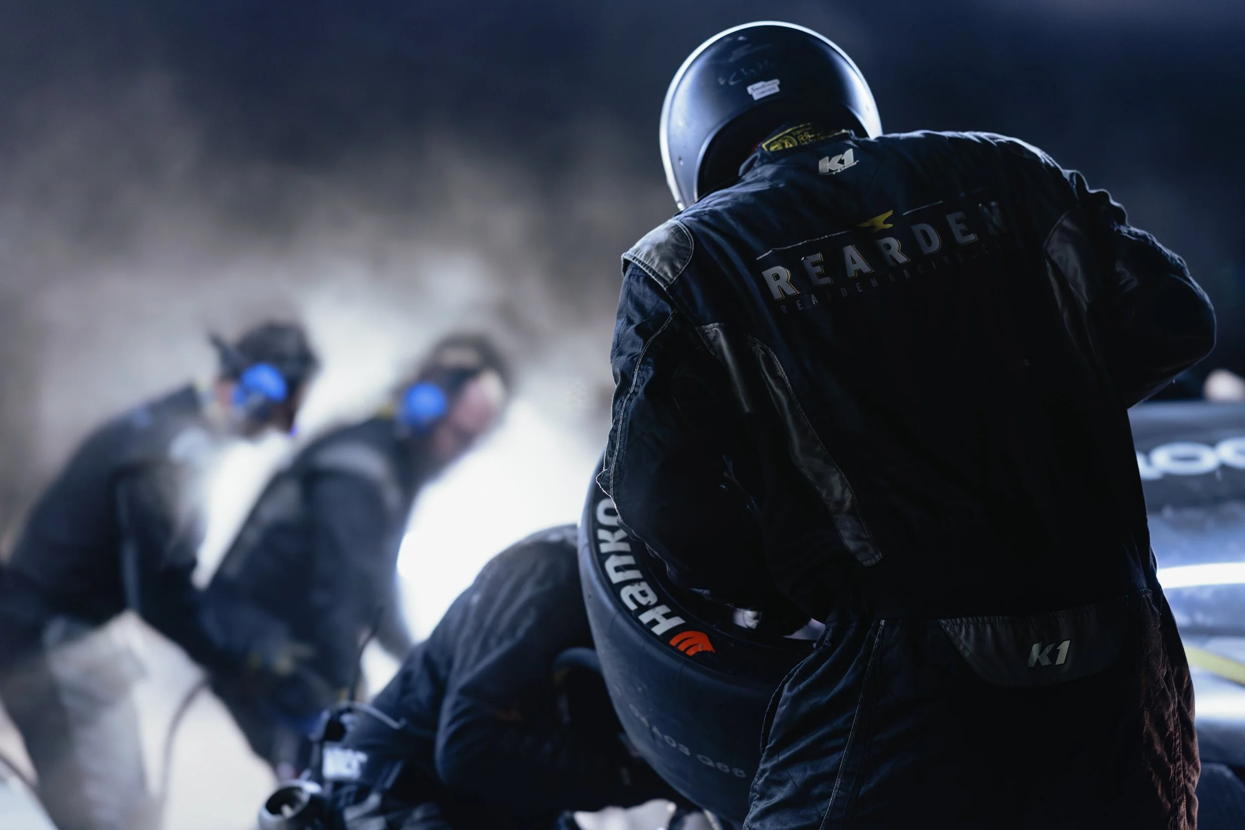 A race team crew member holds a tire while performing a tire change in a pit stop during an endurance race.