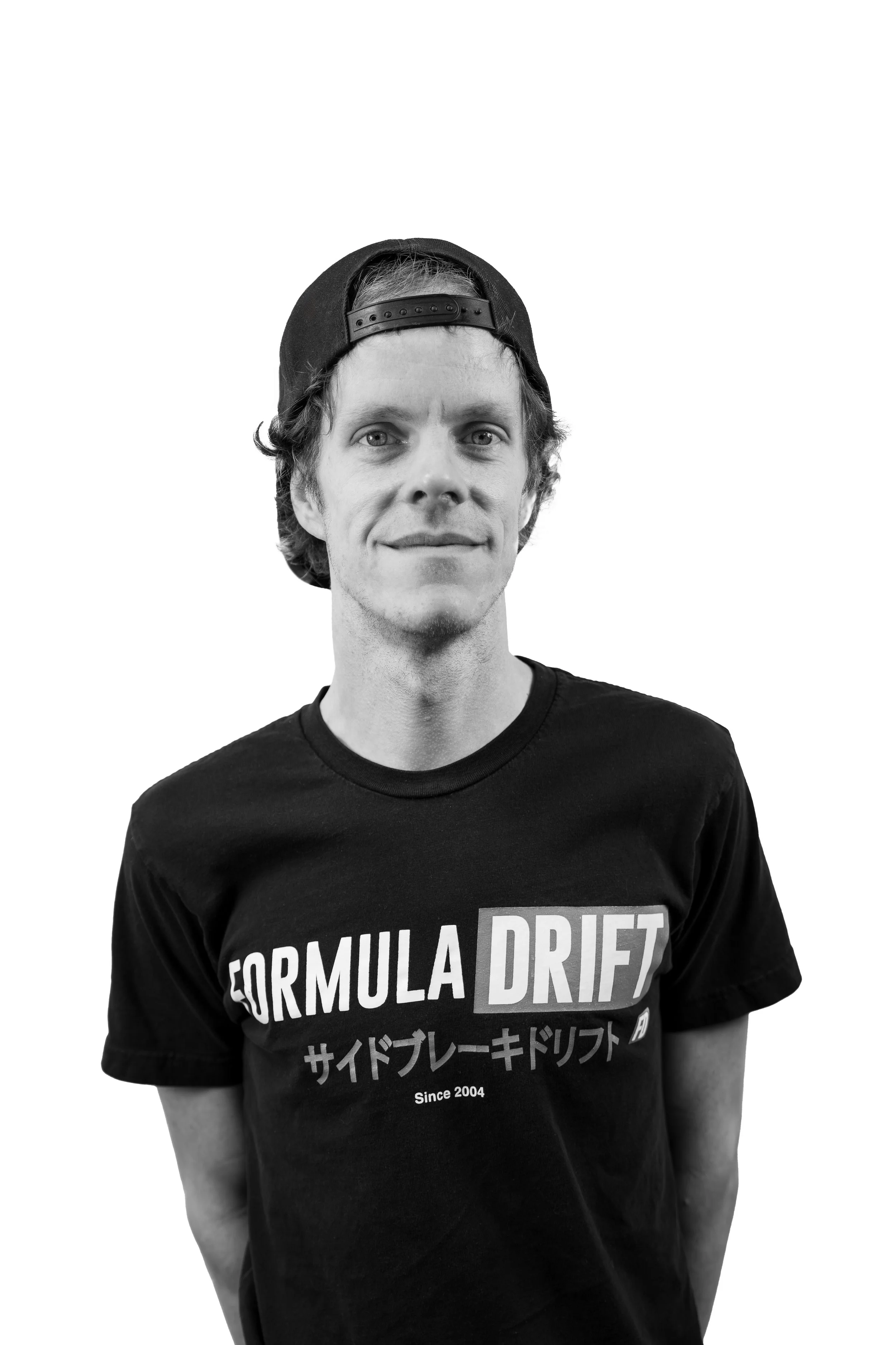 A young man wearing a backward baseball cap and a T-shirt that says 'FORMULA DRIFT' with Japanese characters and 'Since 2004' on a plain white background.