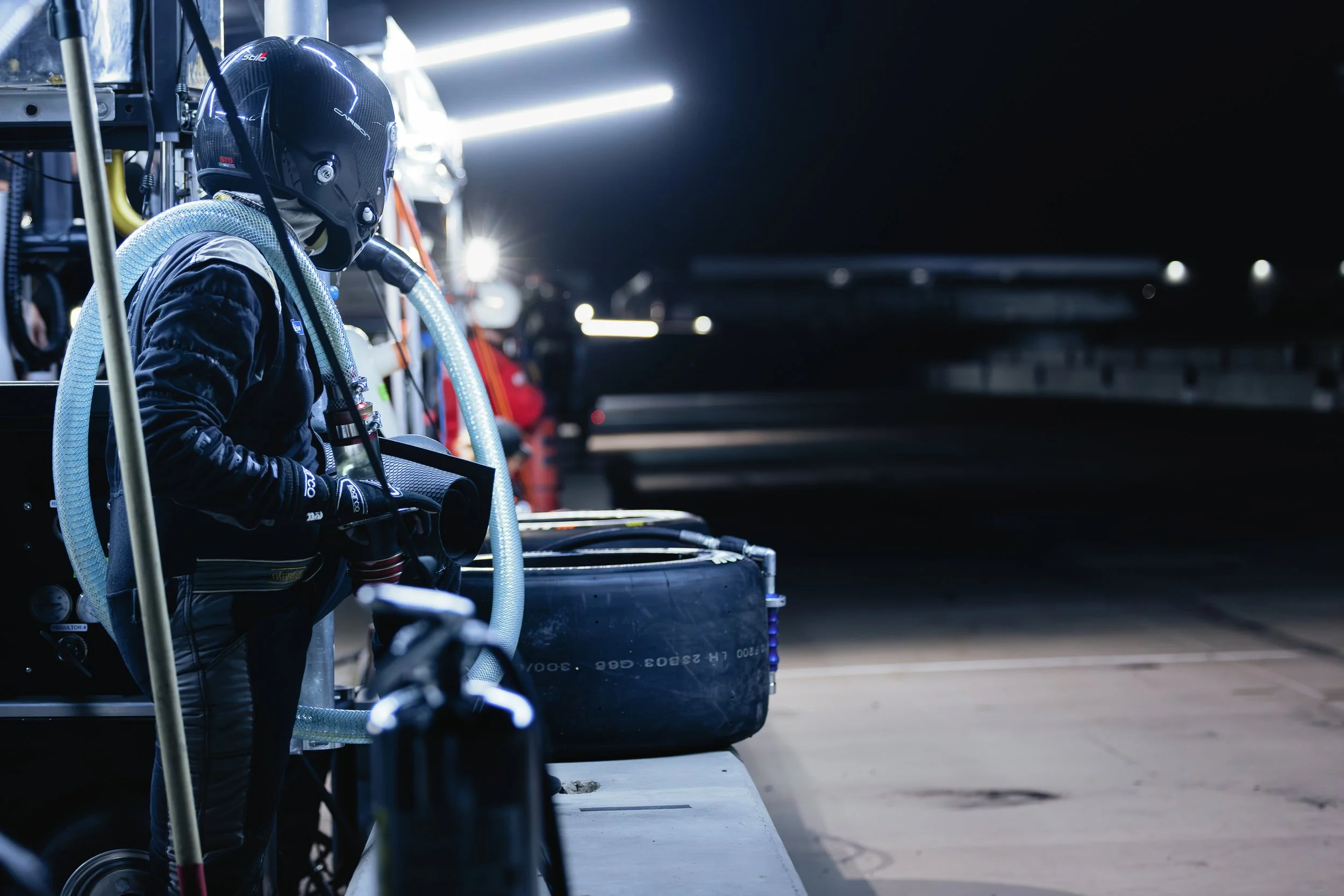 A race team crew member waits for a car to pit. Image captures the crew member holding the fuel hose for refueling.