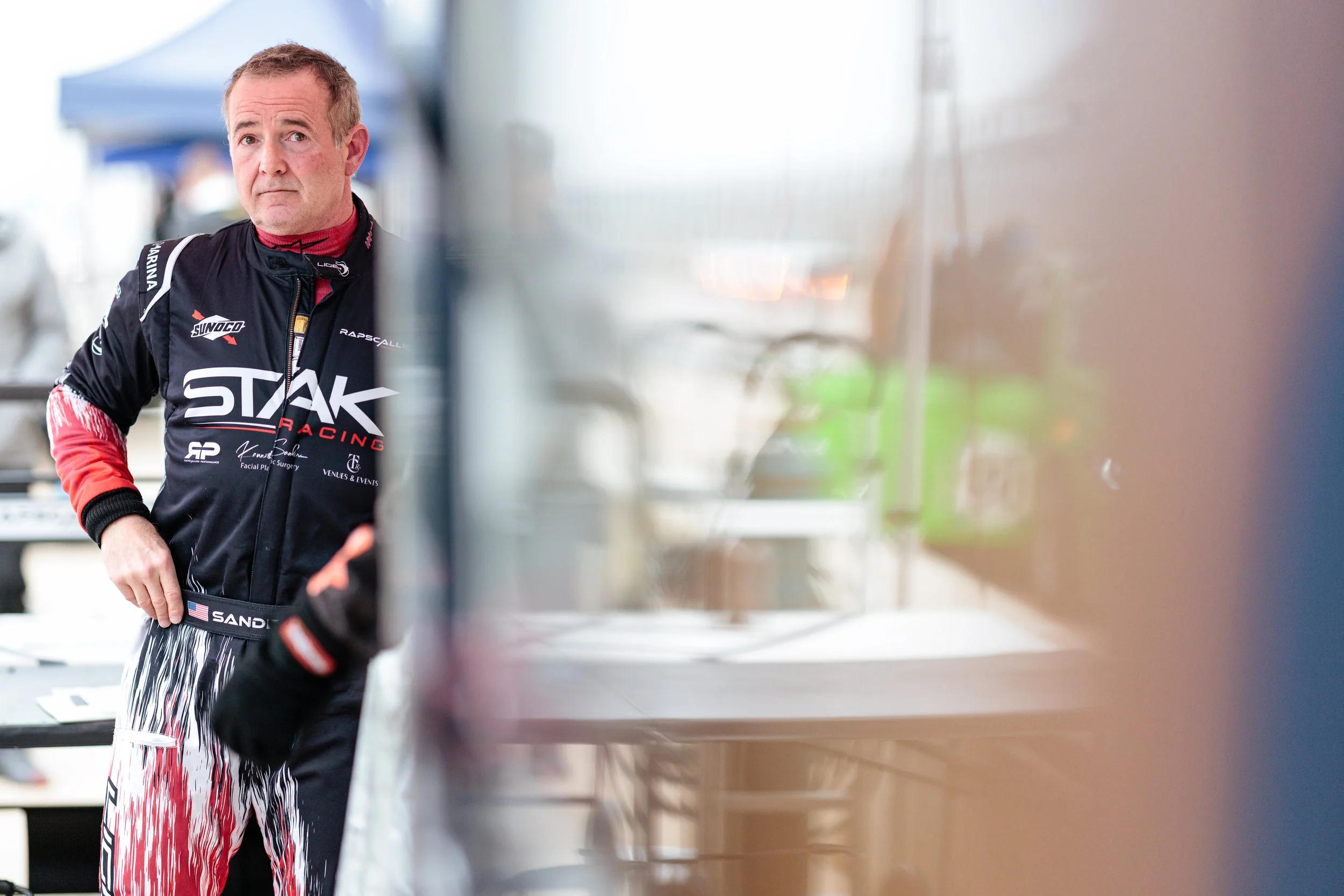 A race car driver standing in pit lane during an endurance race waiting for the next driver change.
