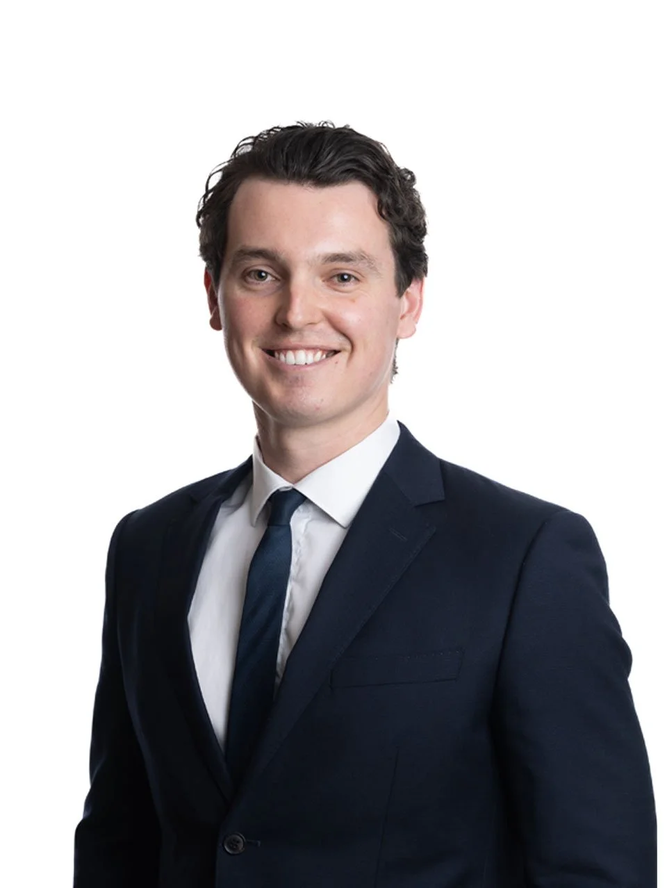 Tom Brand,  in a business suit with a white shirt and dark tie, standing against a plain white background.