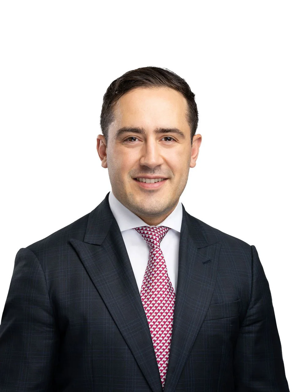 Headshot of a man in a dark plaid suit, white shirt, and red patterned tie, smiling against a white background.