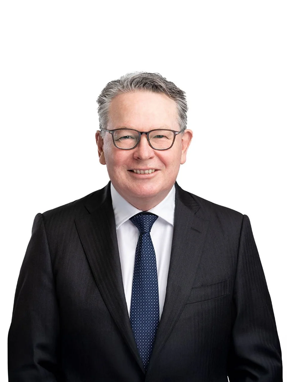 Portrait of a middle-aged man in a black suit, white shirt, and navy tie, smiling, with glasses, against a white background.
