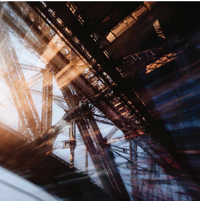 Abstract view of a steel bridge or tower under a sunset, with metal beams and structure creating intricate geometric patterns.