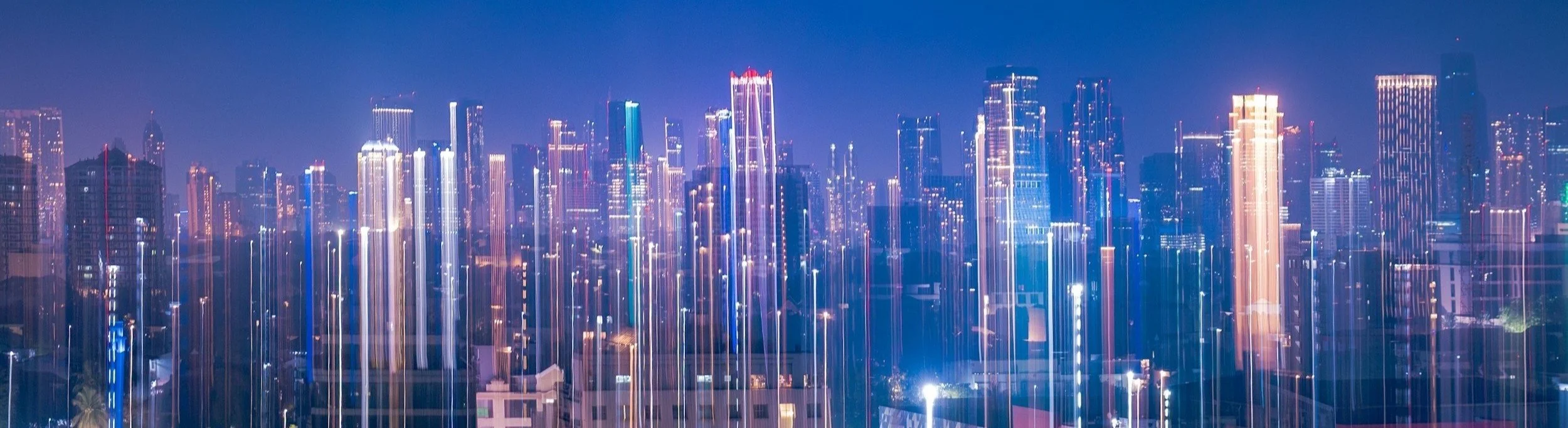 Nighttime city skyline with illuminated skyscrapers and light trails.