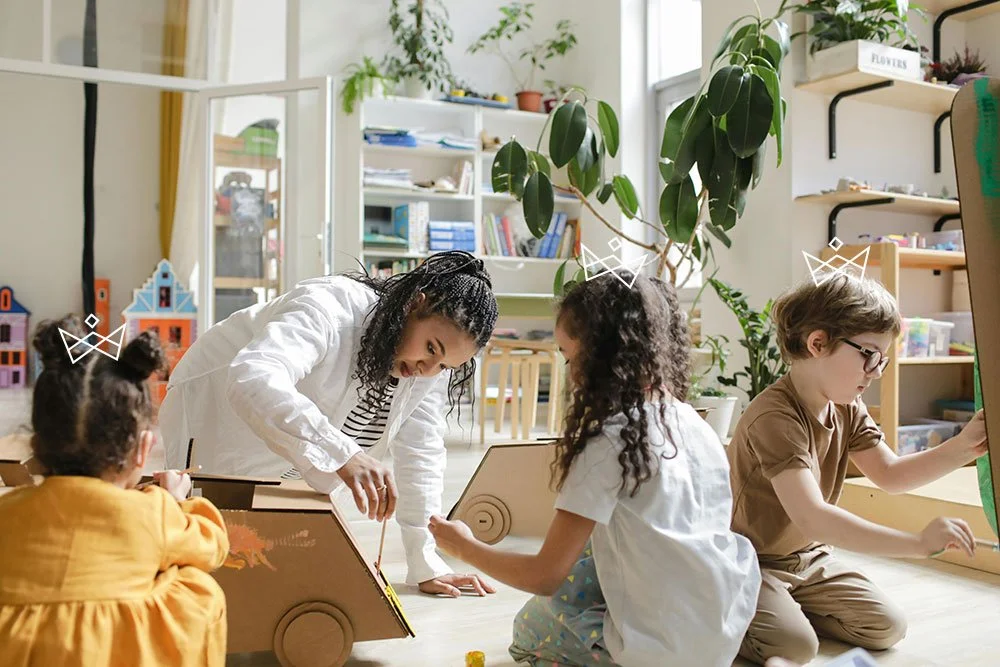 Teacher and children playing with cardboard roll toy in classroom with plants and shelves.