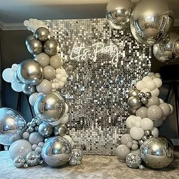 Balloon arch with silver, white, and metallic balloons in front of a silver sequin backdrop that reads 'Let's Party' for a celebration or party event.