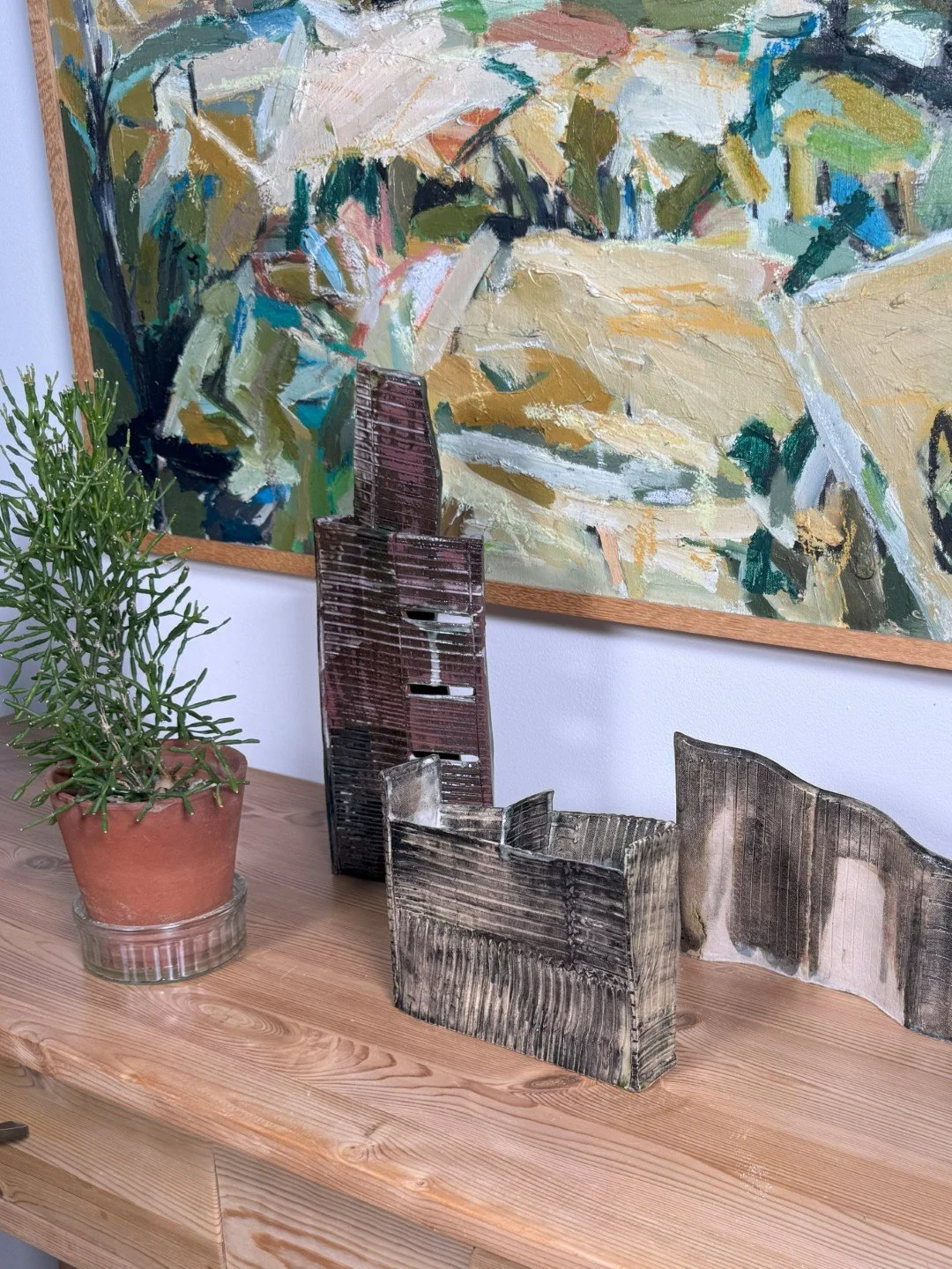 Skyline 4 and other sculptures by ceramic Artist Cristina Lorenzet on a side table with beautiful painting in the background.