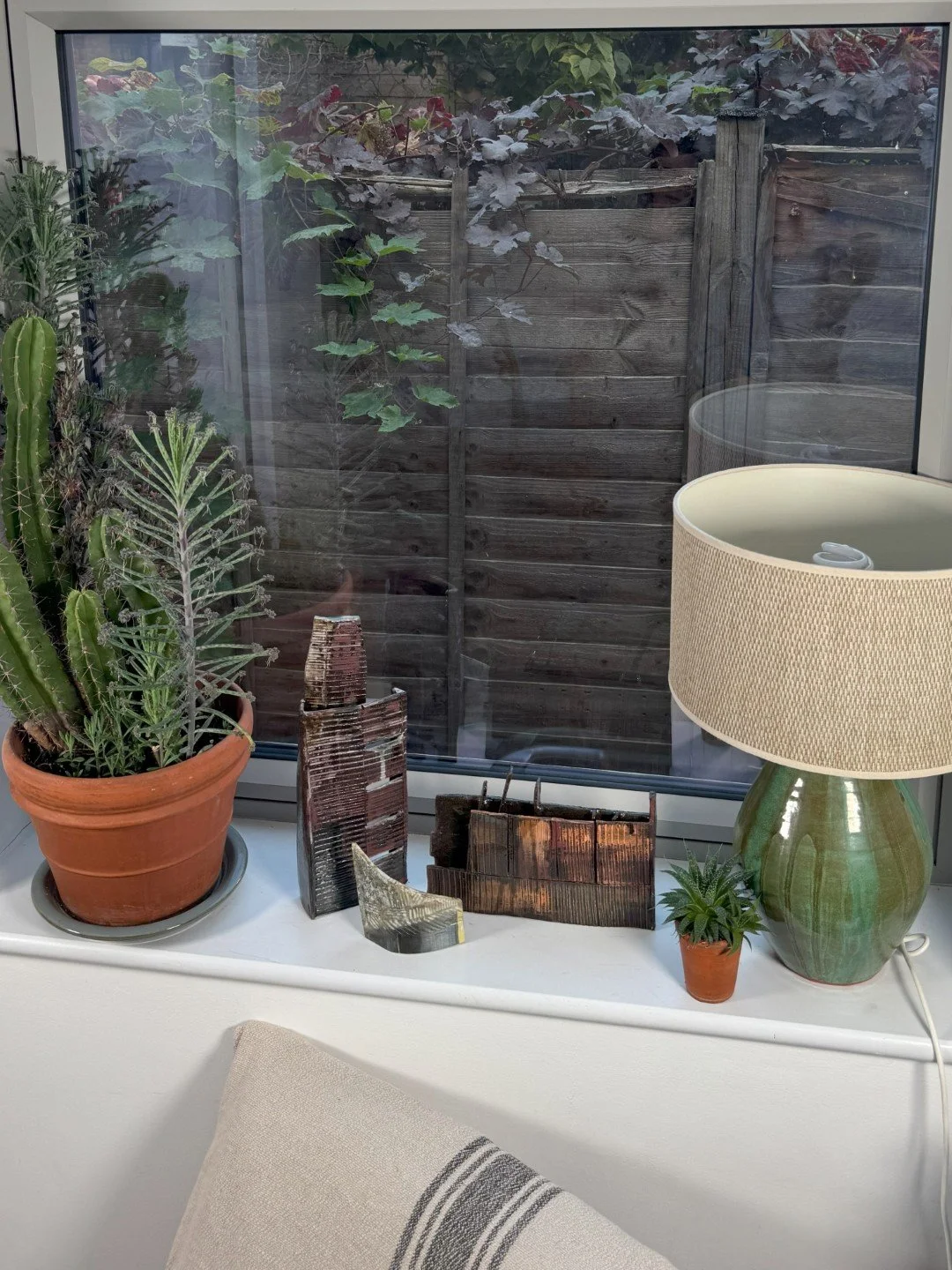 Skyline 4 and other sculptures by ceramic Artist Cristina Lorenzet on a windowsill with beautiful plants and lamp.