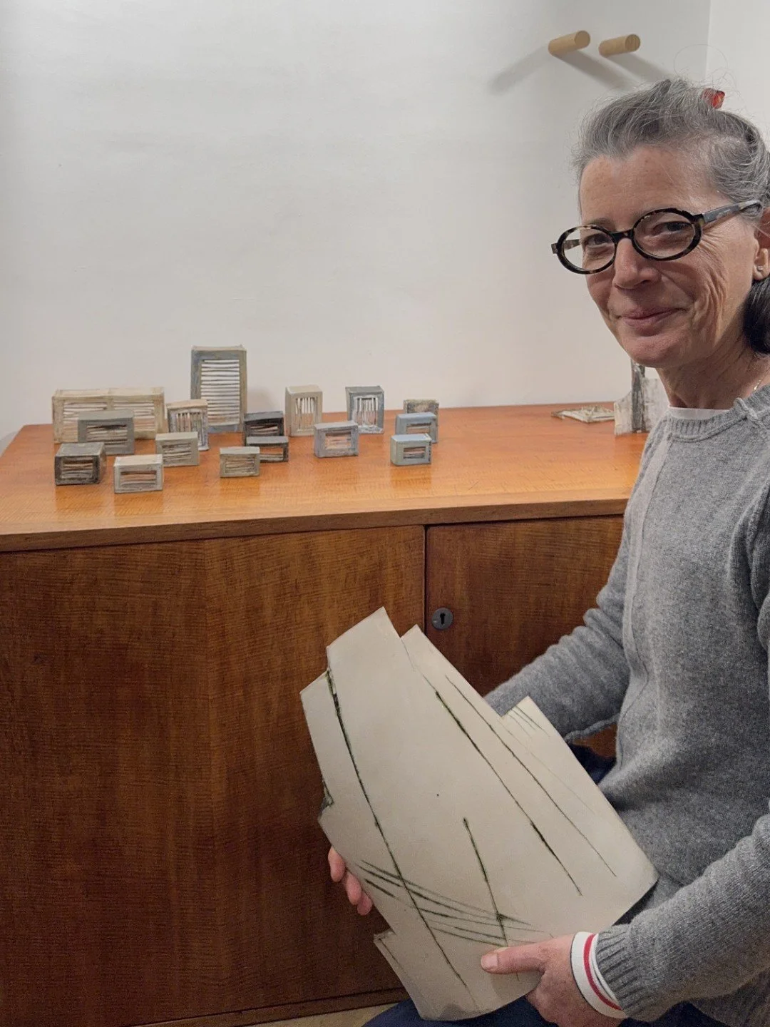 London Façade 1 white stoneware sculpture held in the arms of ceramic Artist Cristina Lorenzet, in front of other artworks.