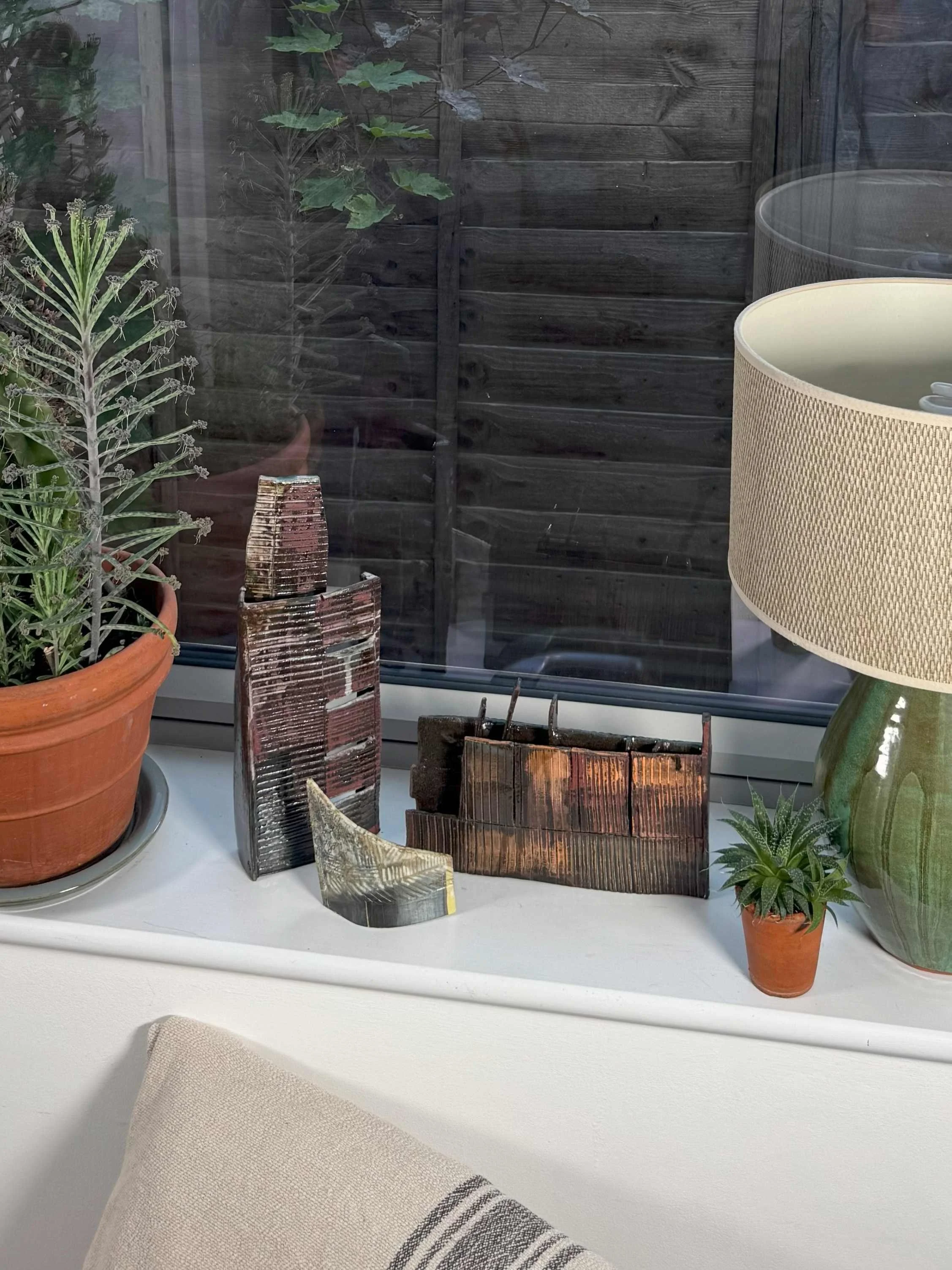 Skyline 1 red stoneware sculpture by ceramic Artist Cristina Lorenzet displayed on a windowsill with other artworks.