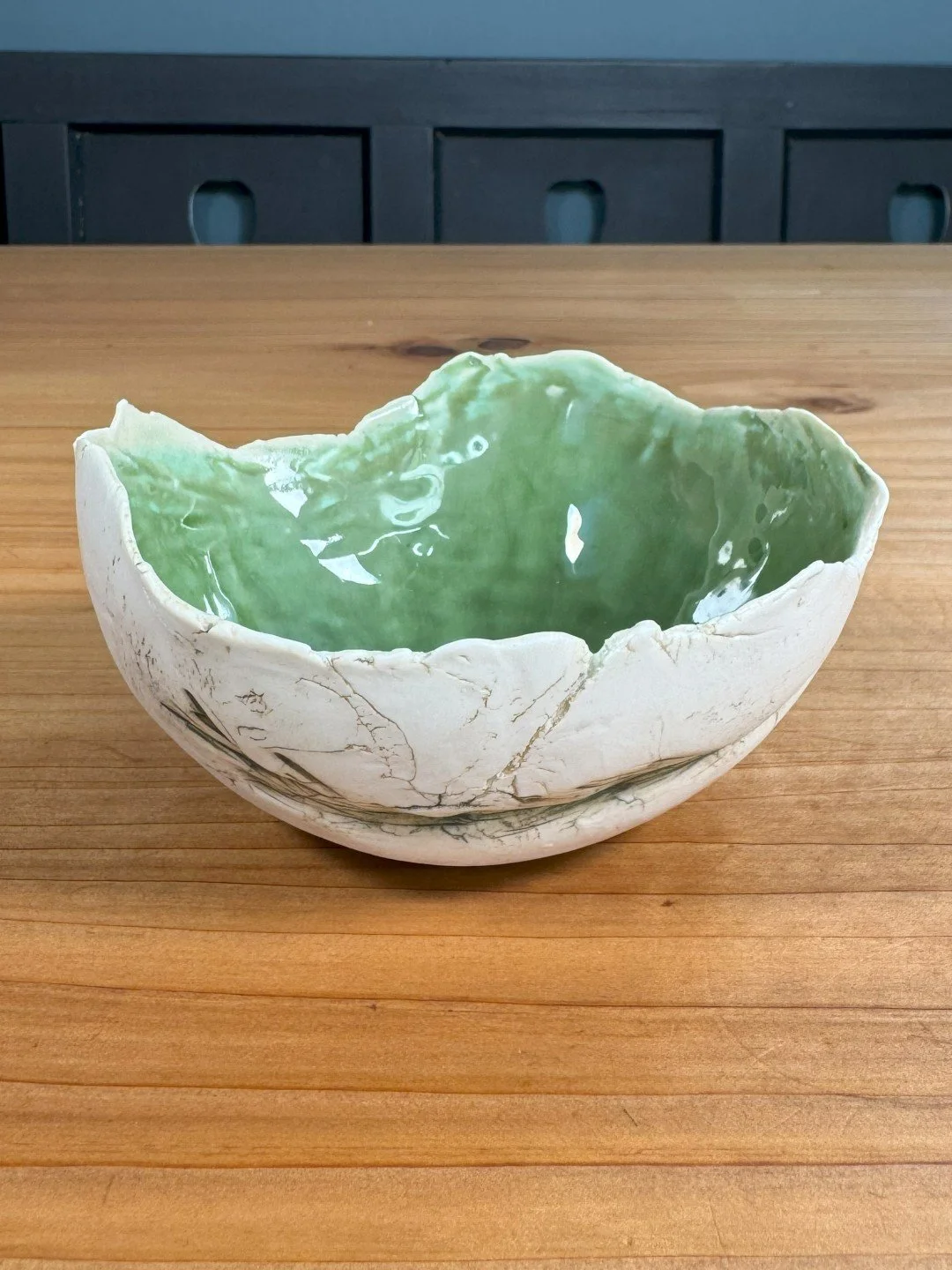 Small rough-edged bowl by Artist Nupur Narain DeTar, with green food-safe glaze inside and a rosemary imprint on the outside.