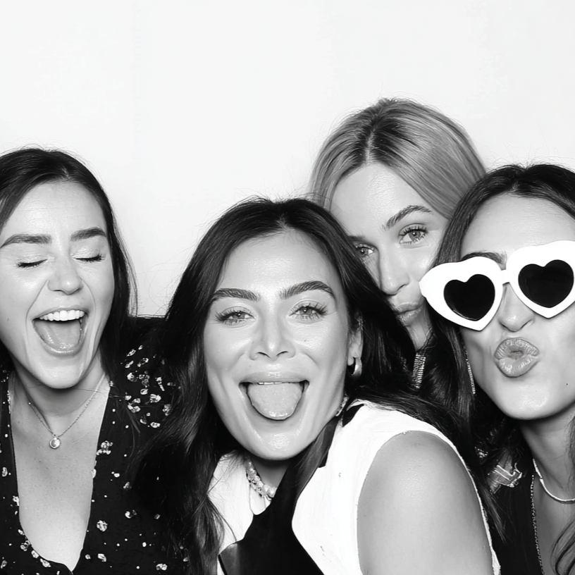 Cťyri zeny spolu pozuji a delaji vtipne vyrazy, jedna z nich ma slunecni bryle ve tvaru srdce.