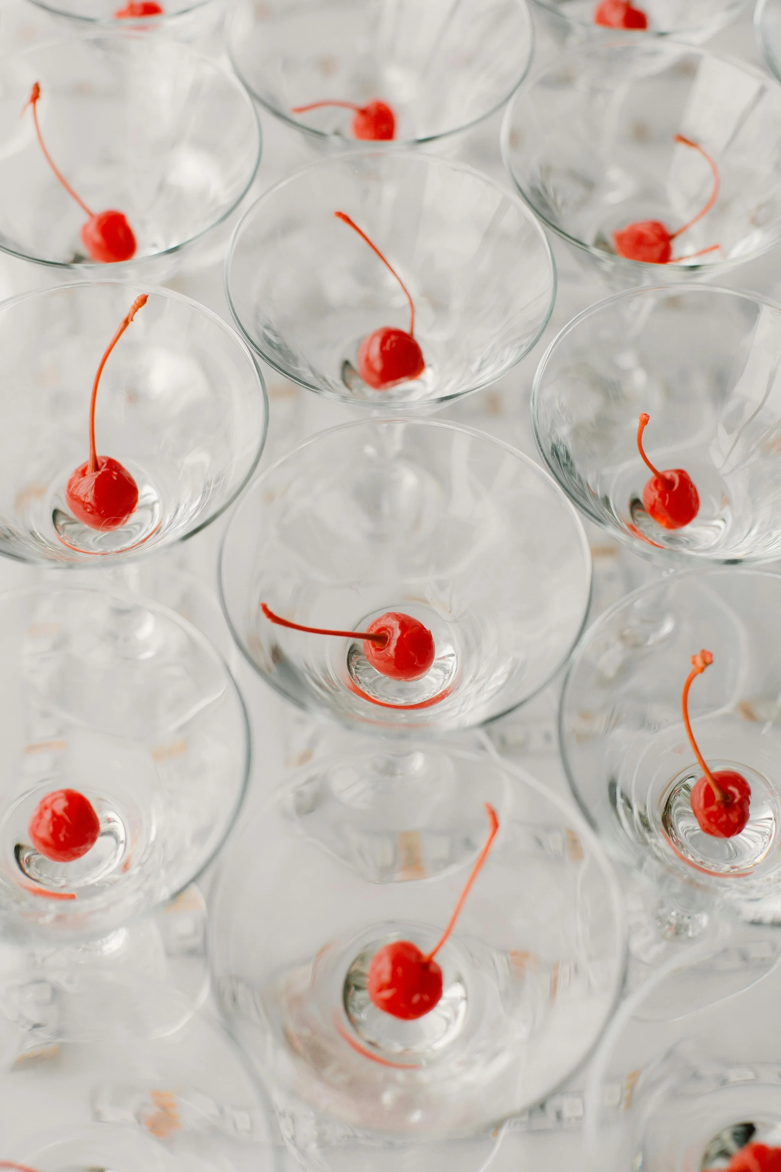 Multiple empty champagne glasses with maraschino cherries placed at the bottom of each glass, view from above.