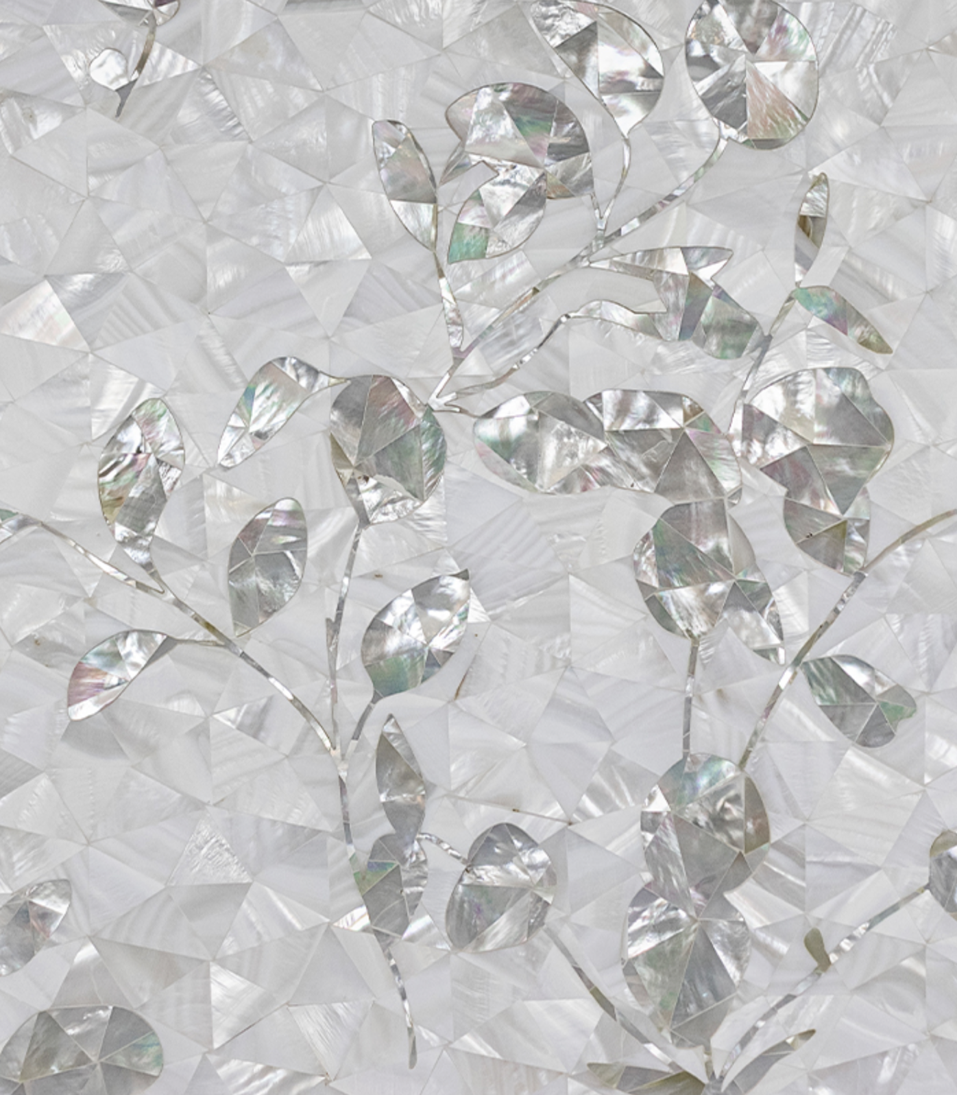 Close-up of a decorative surface with iridescent, faceted, mother-of-pearl leaves and branches set against a textured pearl background.