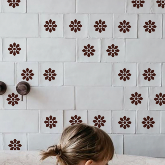 Close-up of a wall decorated with white tiles and brown flower-shaped stickers, with part of a person’s head visible at the bottom.