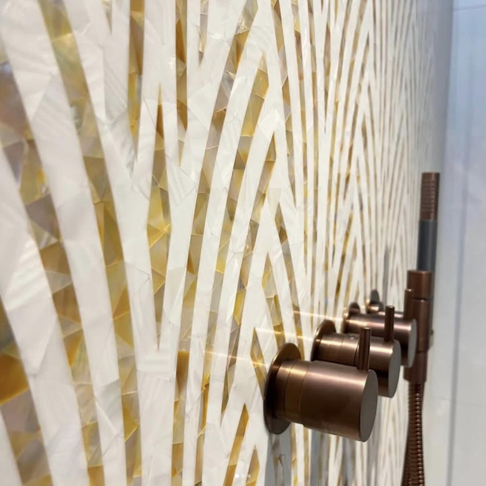 Close-up of a decorative wall with an intricate geometric pattern in white and gold, with copper-colored fixtures visible on the right side.