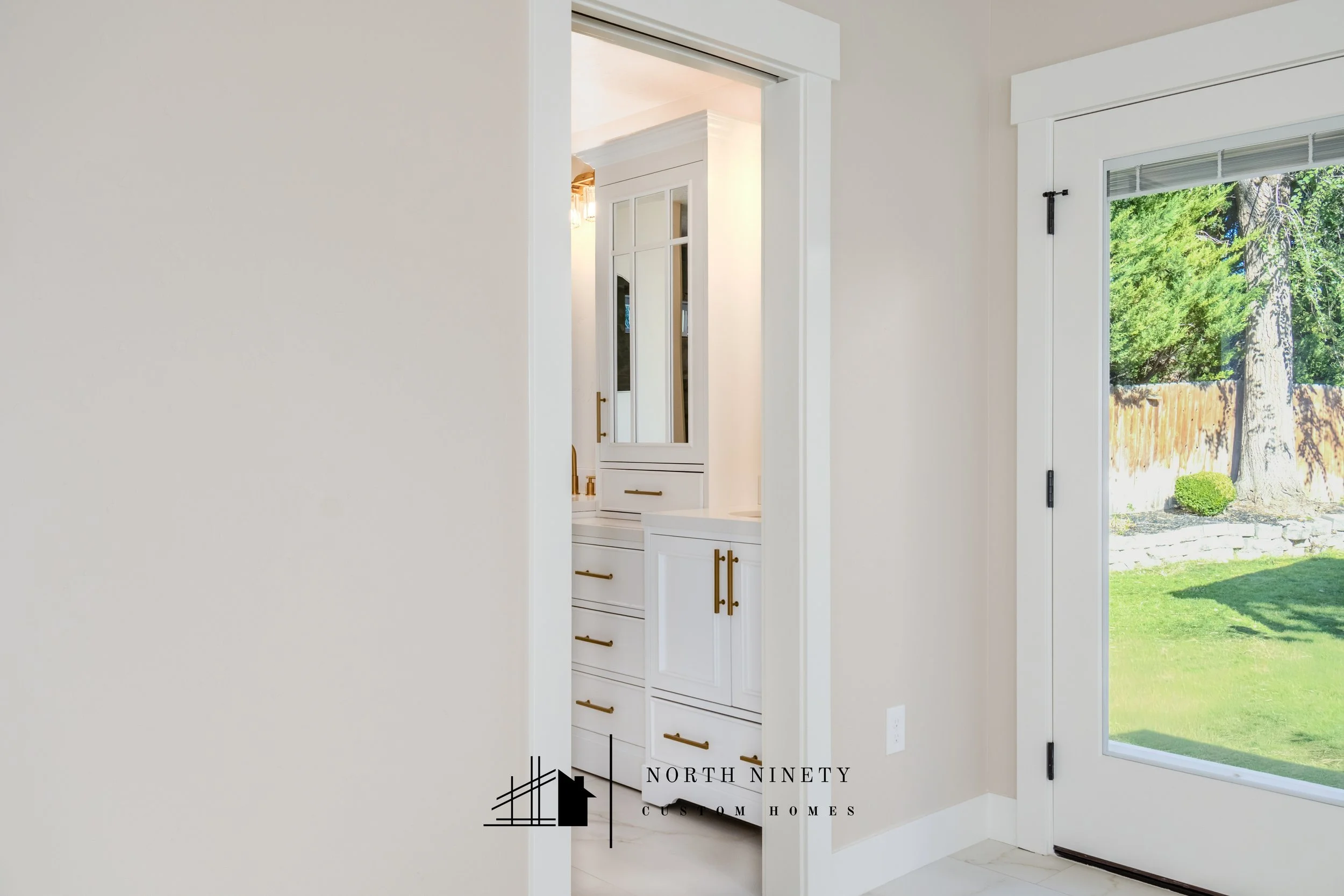 View of a bright kitchen with white cabinetry and a large sliding glass door showing a green backyard. North Ninety Custom Homes | Treasure Valley | Idaho