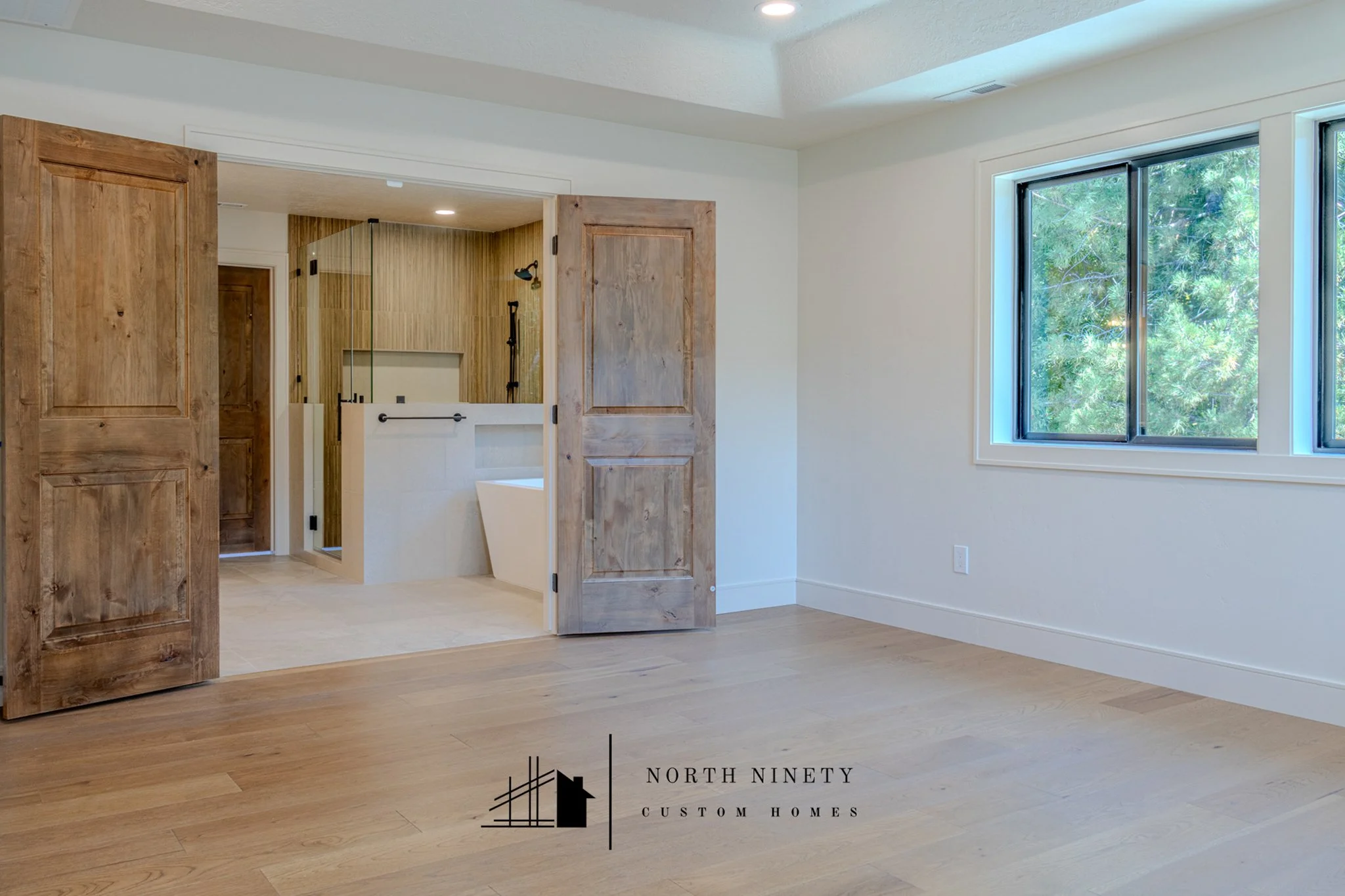 Custom interior features of the Brookwood project, a whole home remodel in Eagle, ID
Interior of a modern house with a wooden sliding door, a large window showing green trees outside, and a bathroom with a glass shower.