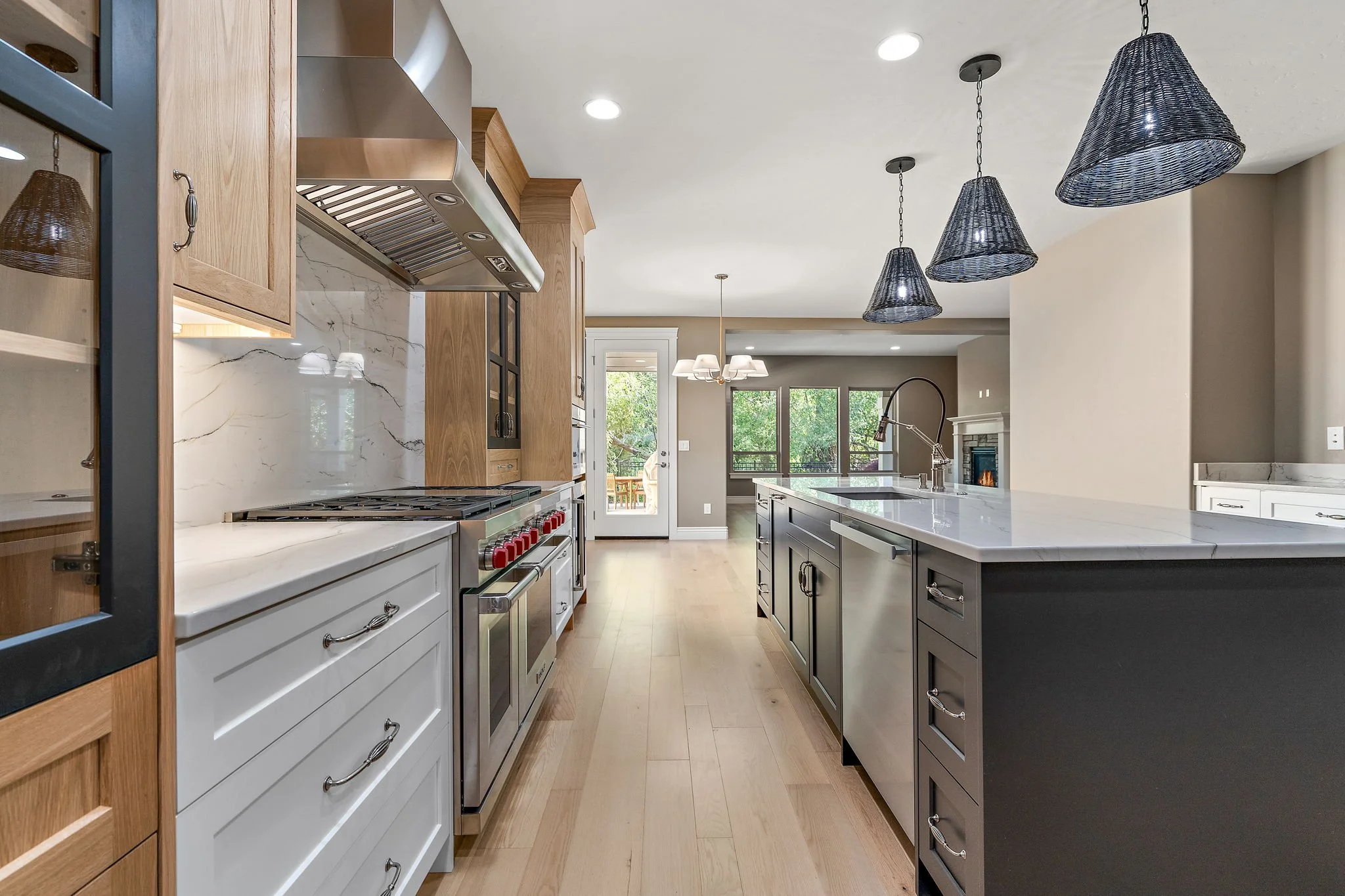 A modern kitchen with a long white marble island, black cabinetry, and built-in appliances. Three black woven pendant lights hang from the ceiling. There are large windows and a luxury feel. Eagle, Idaho. Custom Homes & Remodels by North Ninety 