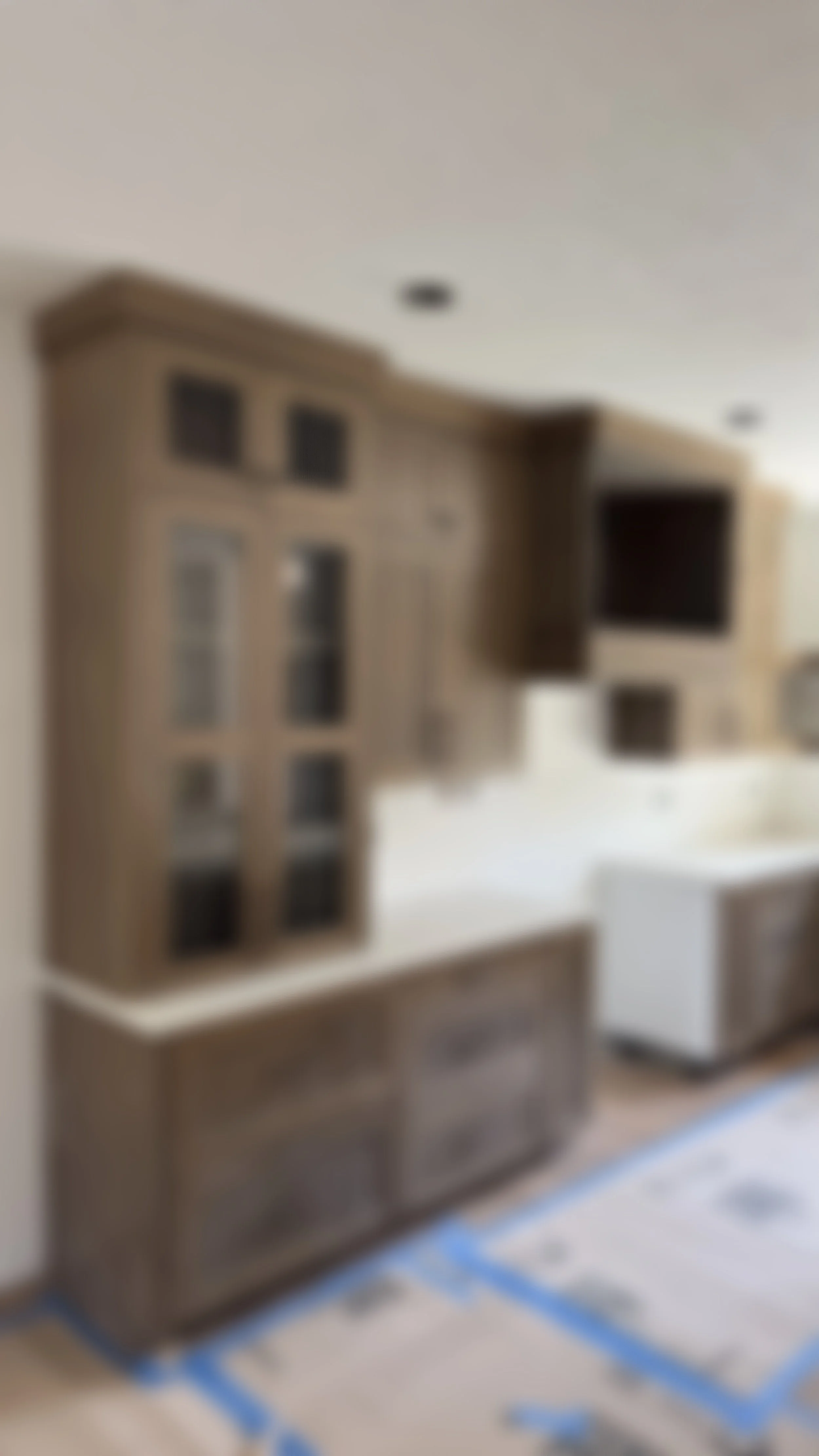 Blurred image of a wooden shelving unit on a white wall with some objects and a white box on the floor.