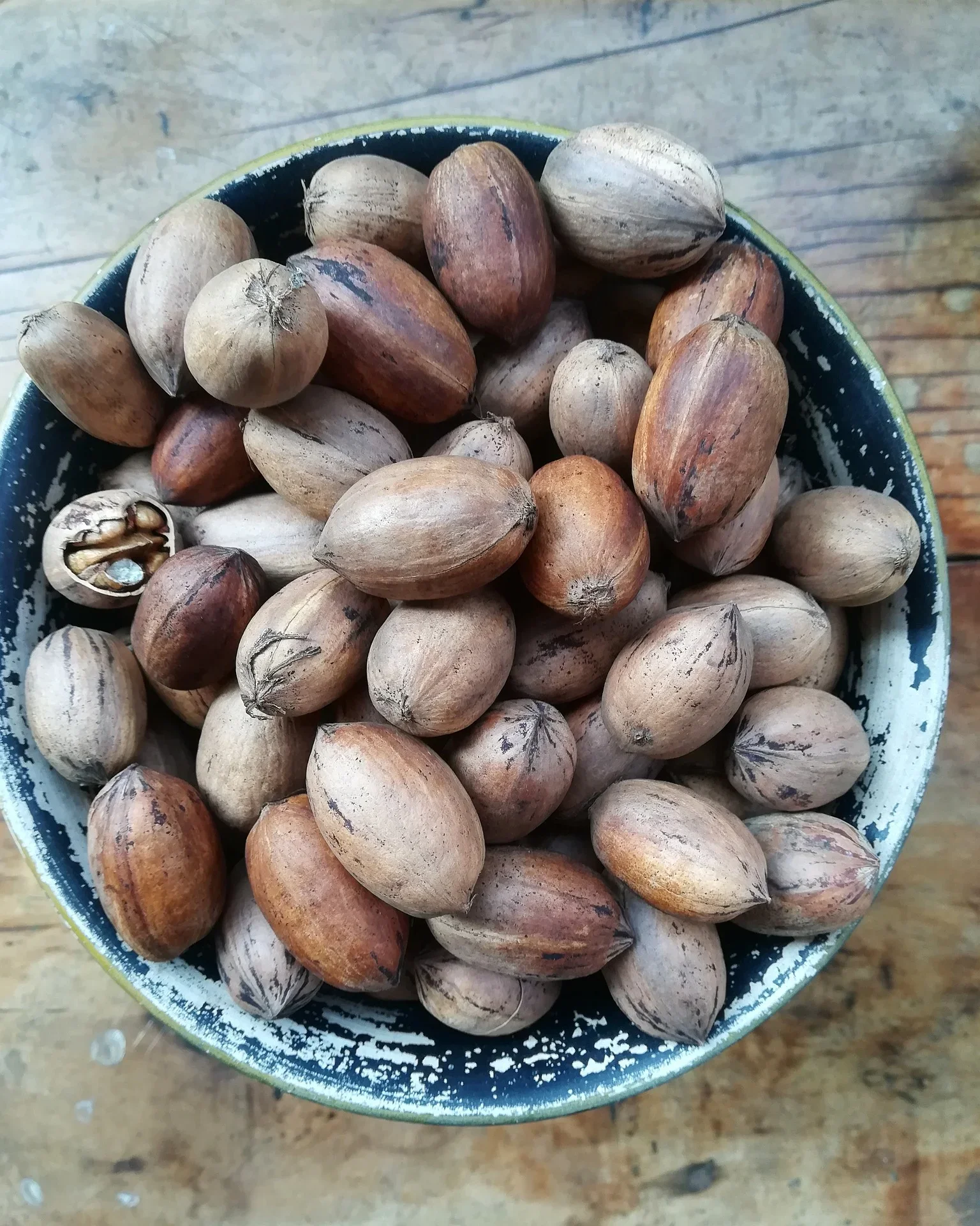 A bowl filled with a variety of forest nuts, including walnuts and other nuts with shells, on a wooden surface.