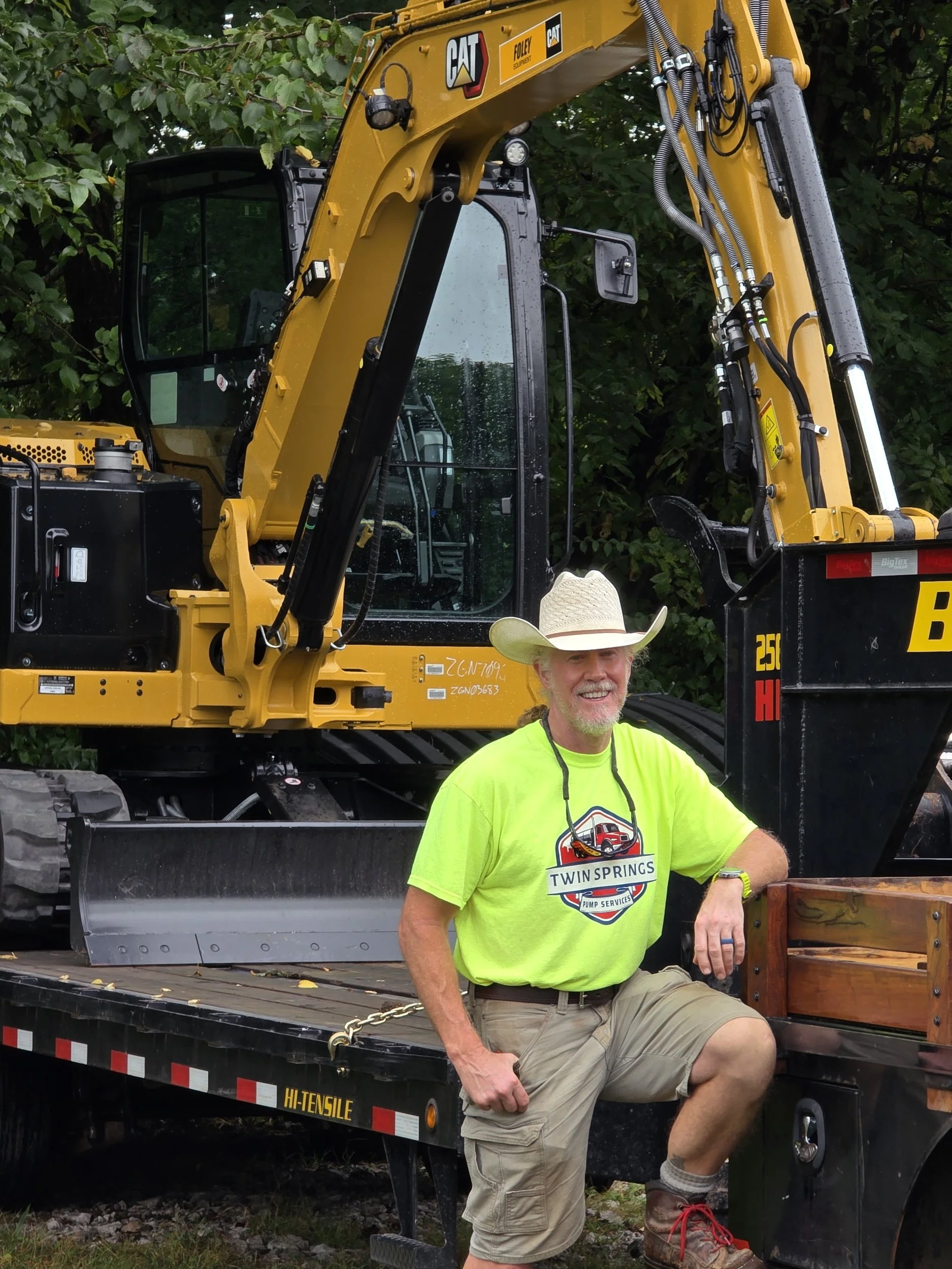 Owner of Twin Springs Pump Services wearing a company shirt beside a CAT excavator.