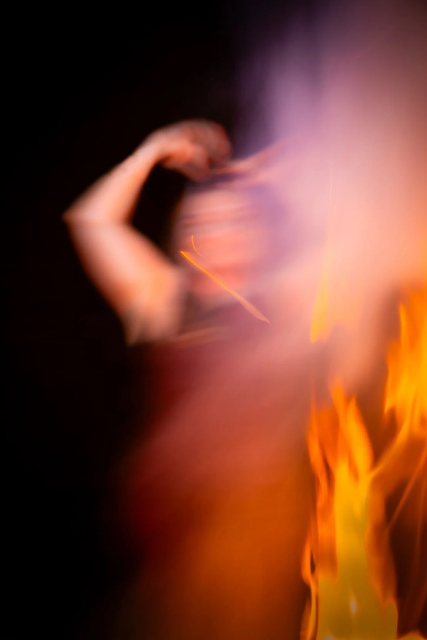 An abstract, blurry photo of a woman with a bright fire and purple smoke or light effects.