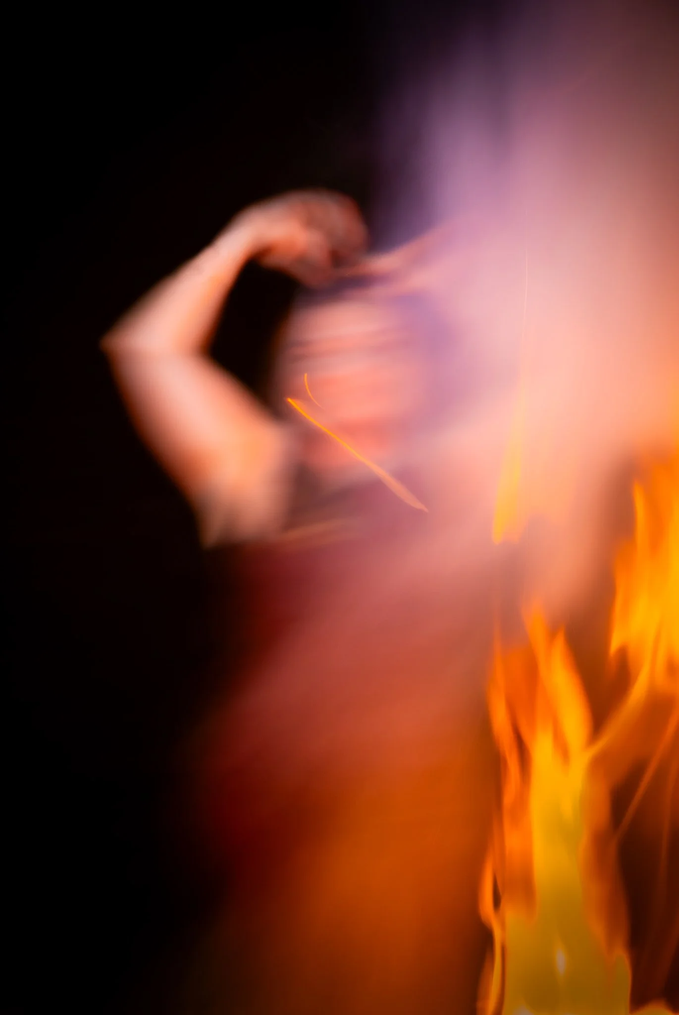 An abstract, blurry photo of a woman with a bright fire and purple smoke or light effects.