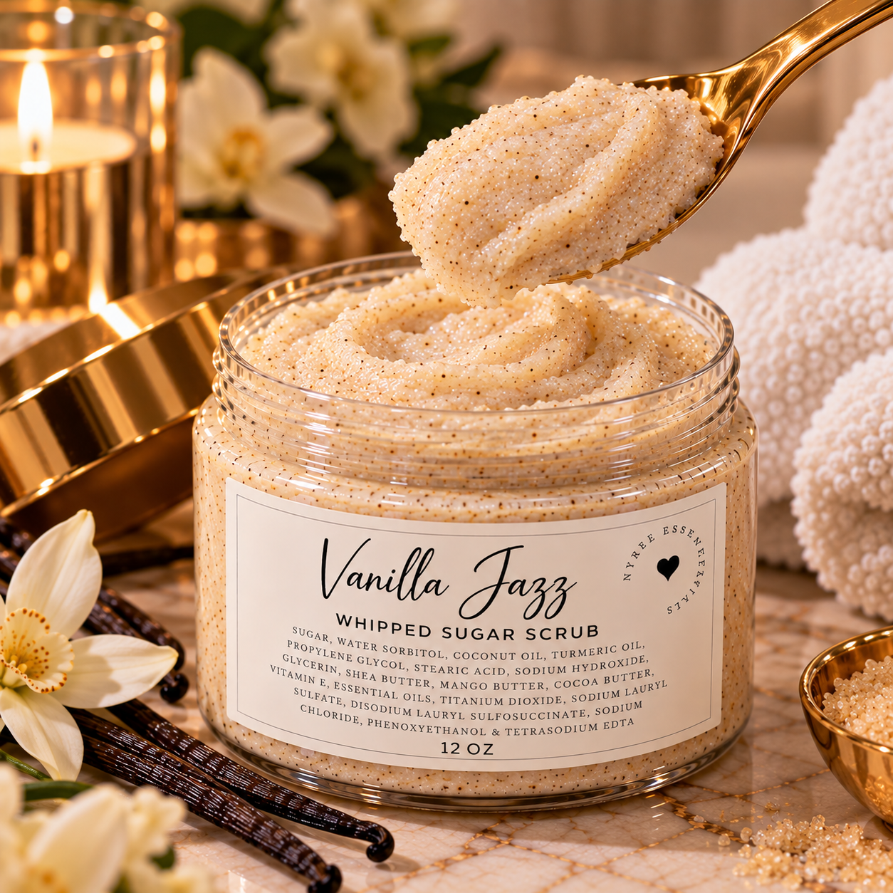 A jar of Vanilla Jazz whipped sugar scrub with a gold spoon scooping some out, surrounded by white flowers, candles, and towels.