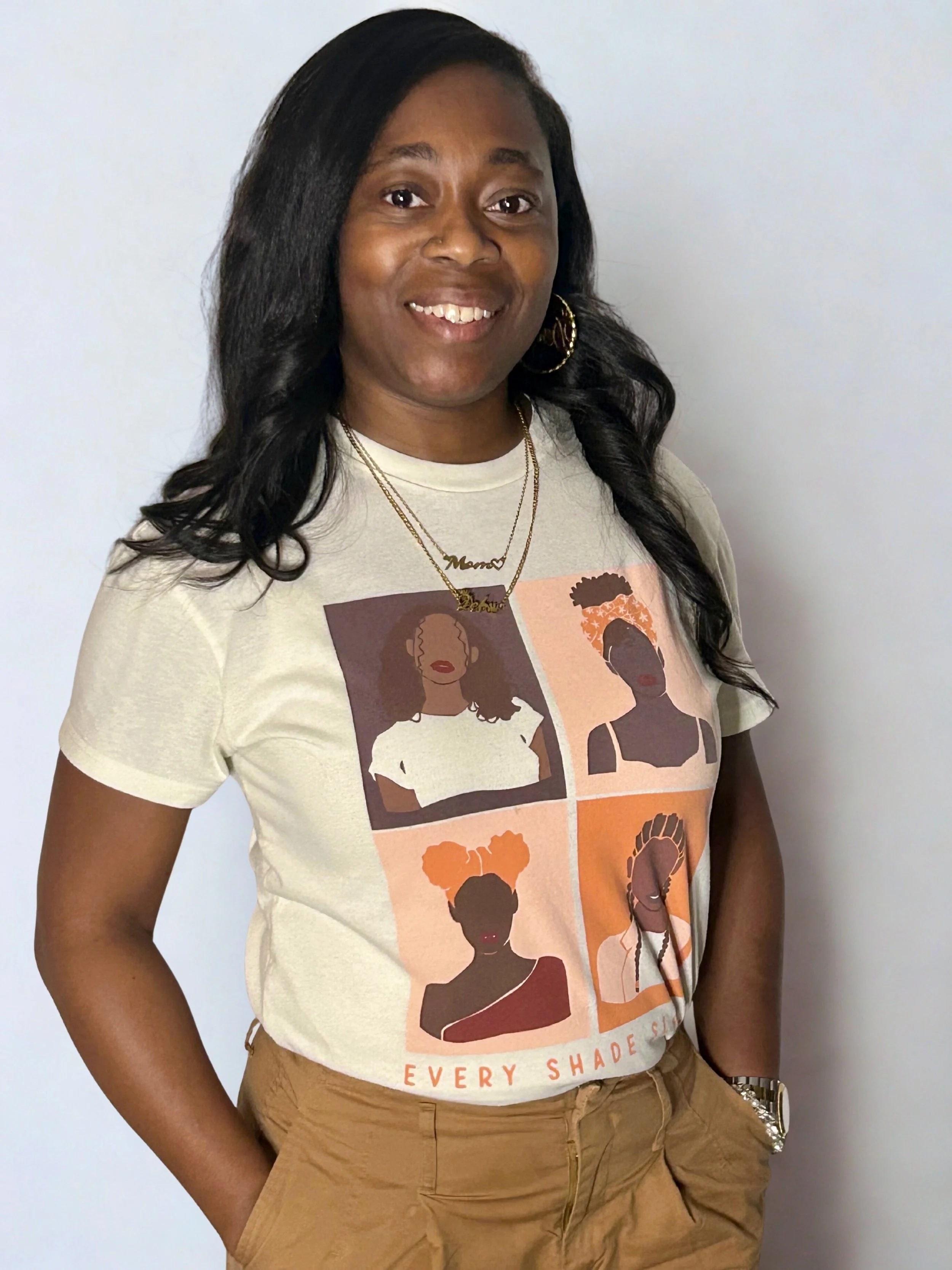 A woman  counselor in Gastonia North Carolina with shoulder-length curly black hair, wearing a yellow shirt, gold necklace, and earrings, smiling against a grey wall background.