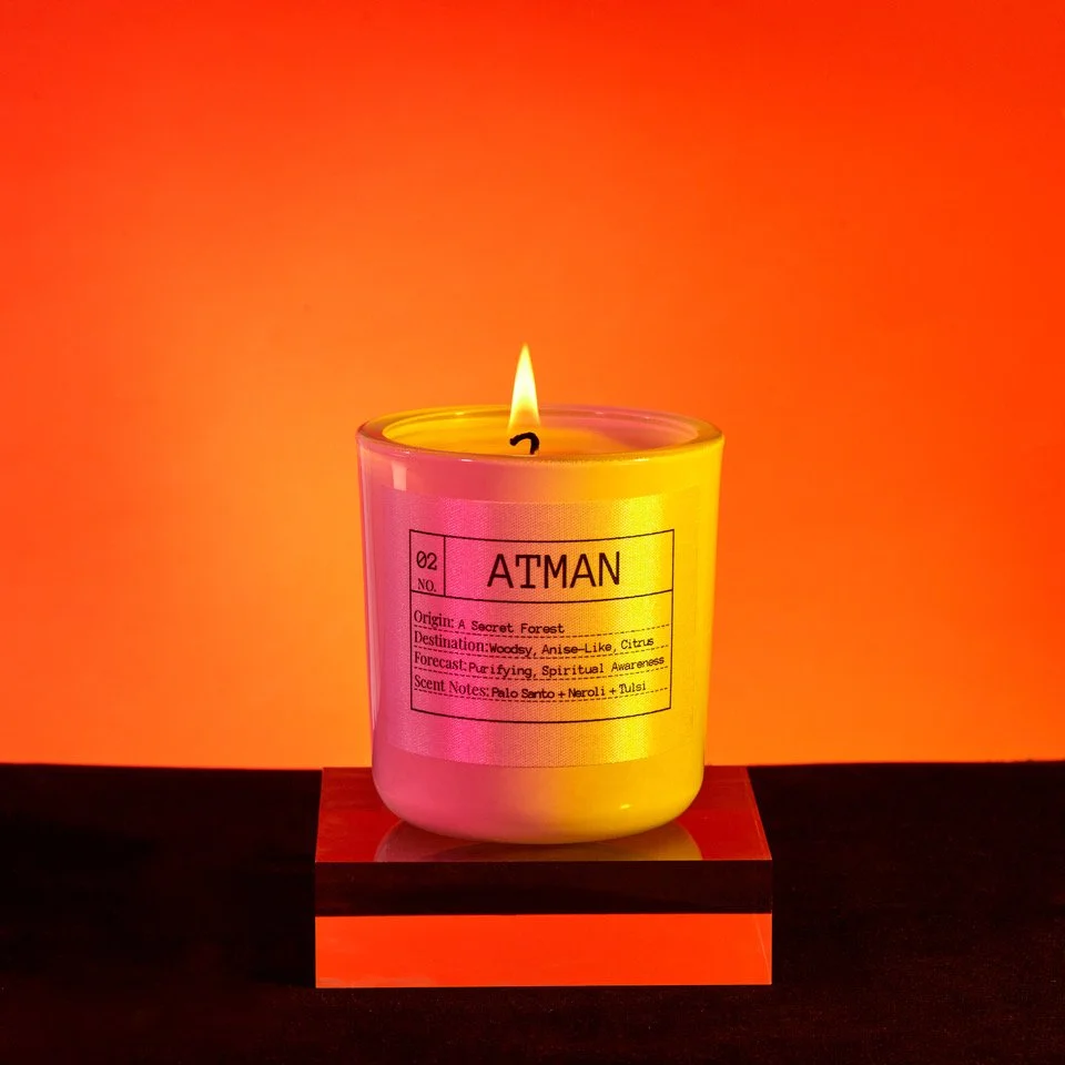 Scented candle labeled "Atman" on a wooden platform against an orange background.