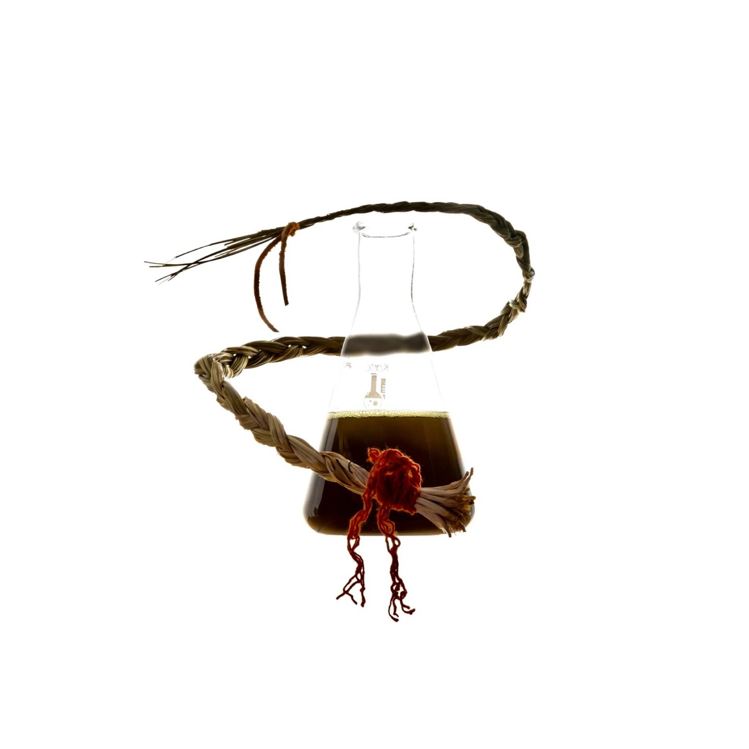 A glass container with a long, braided lock of hair and a piece of red yarn inside, surrounded by a brown woven basket with an open top.