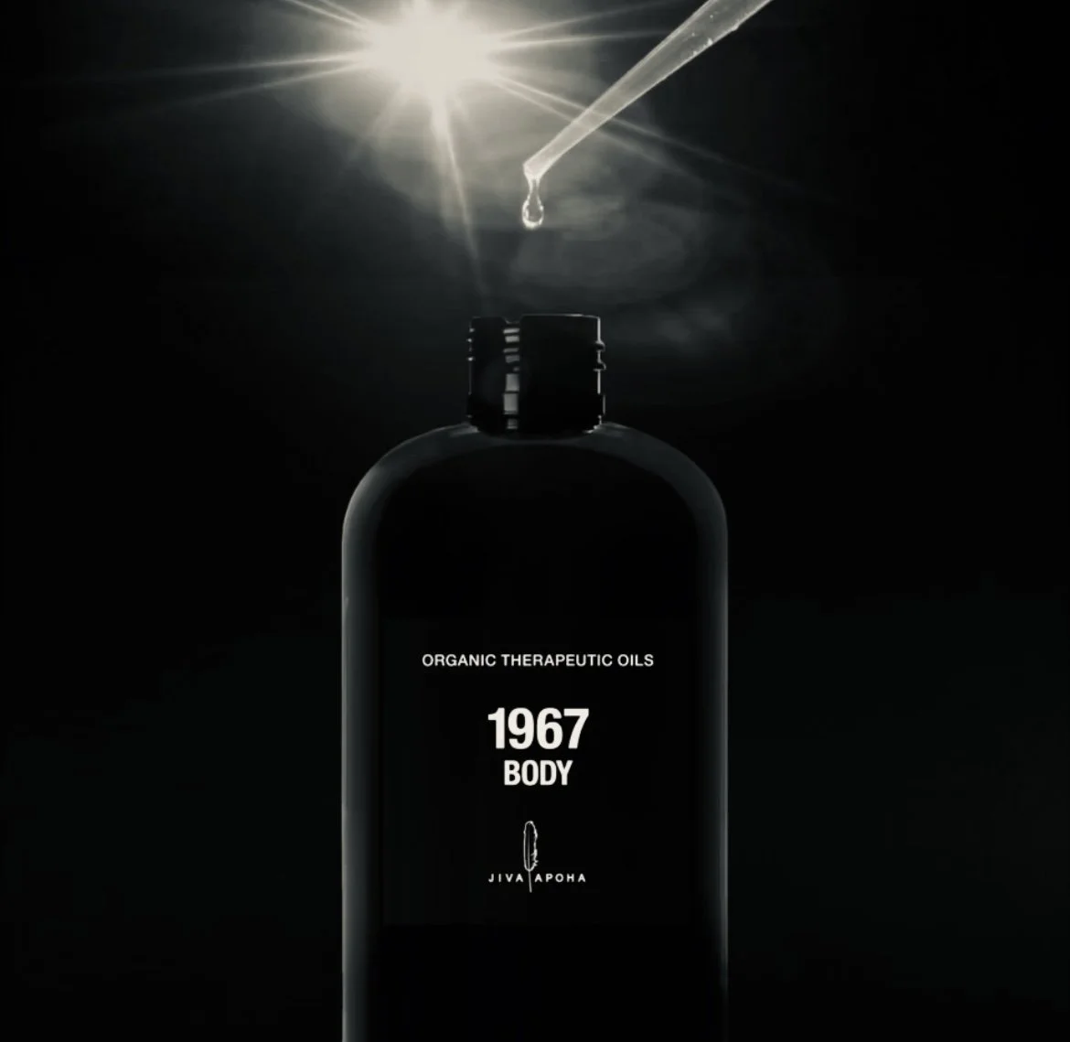 A black bottle of essential oils with a dropper cap, labeled 'Organic Therapeutic Oils 1967 Body' and a small feather graphic, against a dark background with a drop of oil falling from the dropper.