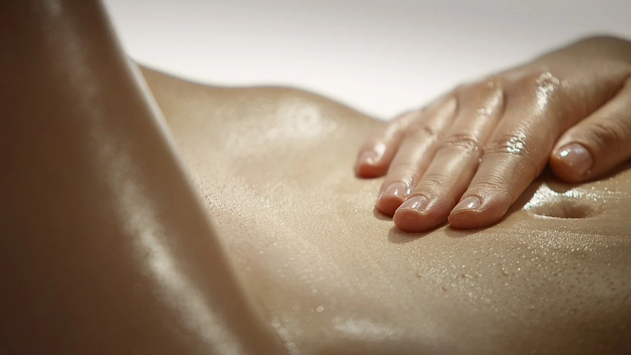 Close-up of a person's hand massaging a person's midsection, with shiny, moisturized skin.