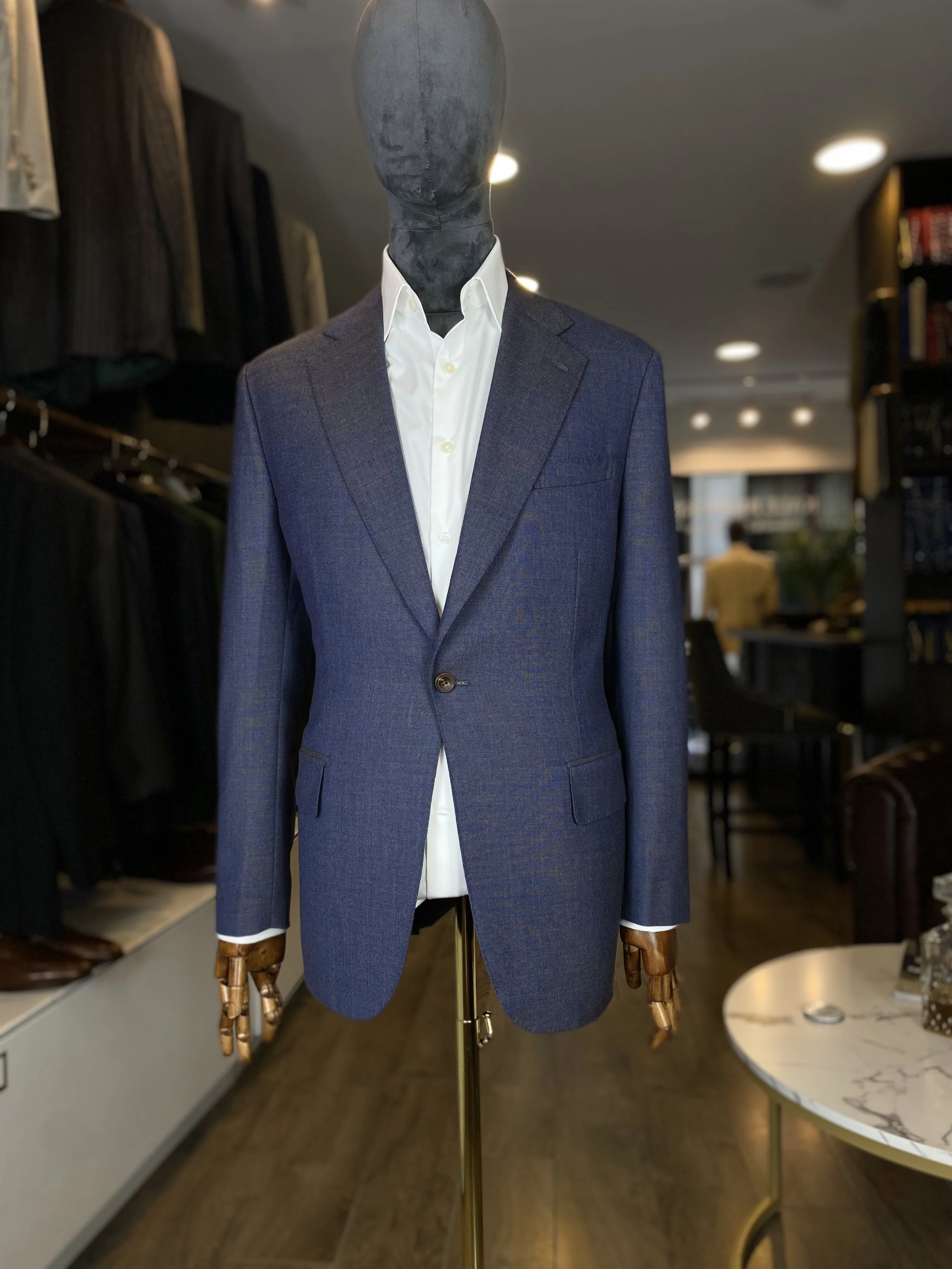 Blue/Grey Loro Piana High-twist Kale bespoke blazer. A sophisticated blue-grey one-button and slanted pockets blazer crafted from luxurious Loro Piana high twist wool, featuring elegant slanted pockets and a clean bespoke silhouette. Displayed on a s