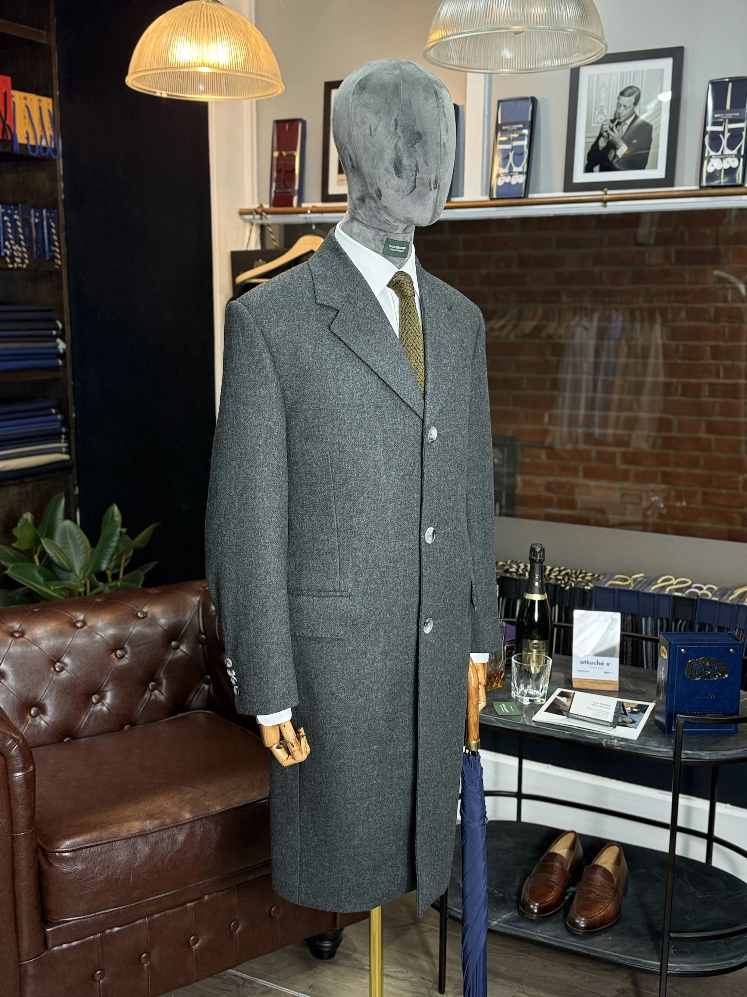 Bespoke Charcoal grey Overcaot No Chest pocket on shop mannequin with a silk knitted green silk tie.This overcaot fabric is 20oz Drim dugdale brothers full hand cut and handmade Kale bespoke Overcoat.Made by Kale Bespoke