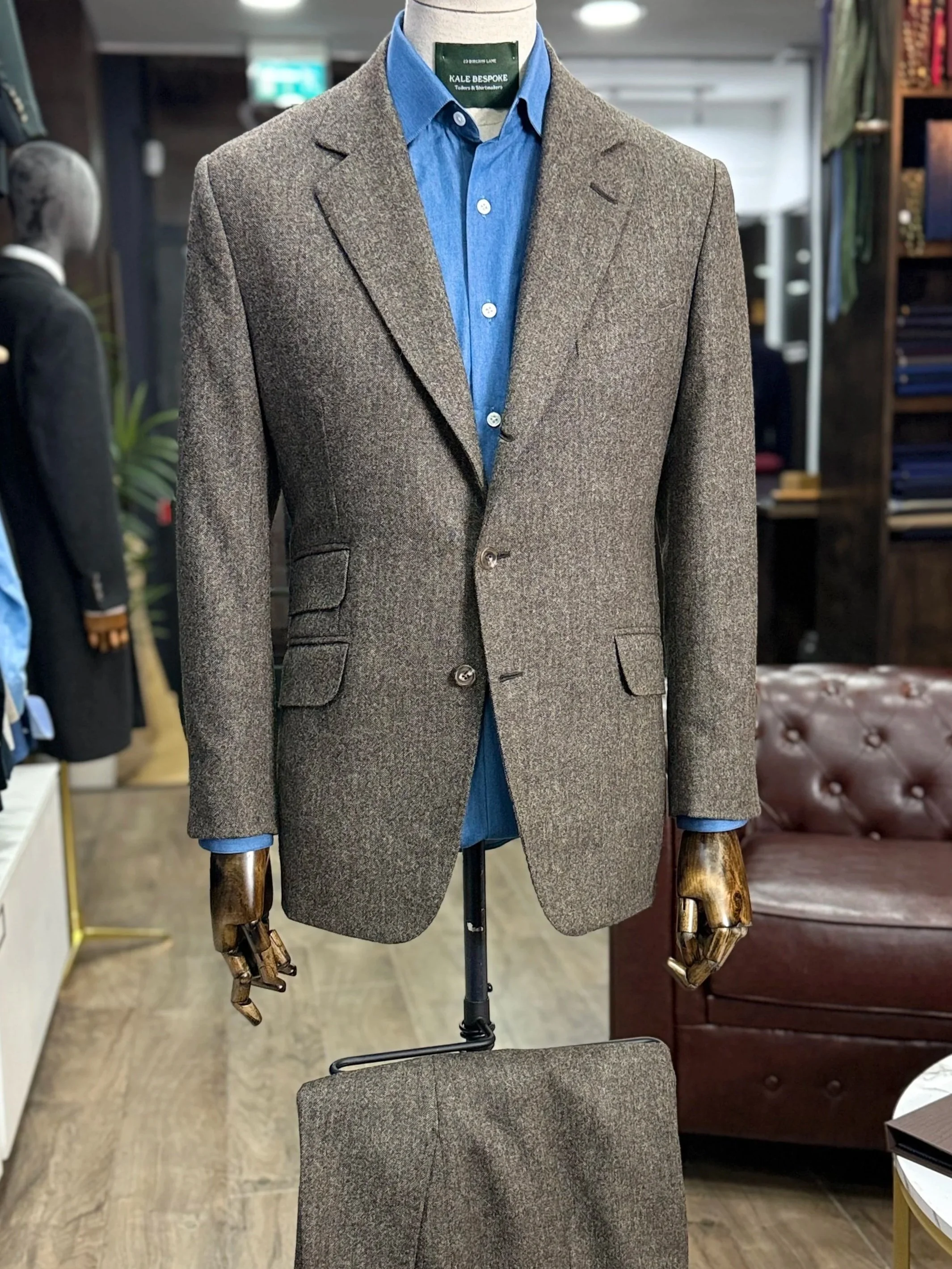 Brown Donegal tweed two-button suit made by Kale Bespoke using Abraham Moon cloth. The tailored jacket features classic notch lapels, slanted side pockets and an additional ticket pocket above, styled with a blue chambray shirt for a refined British 