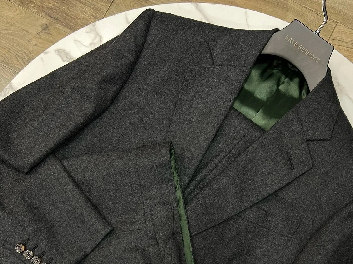 Dark gray tailored suit jacket on a white marble surface with a hanger labeled 'Kale Bespoke'.
